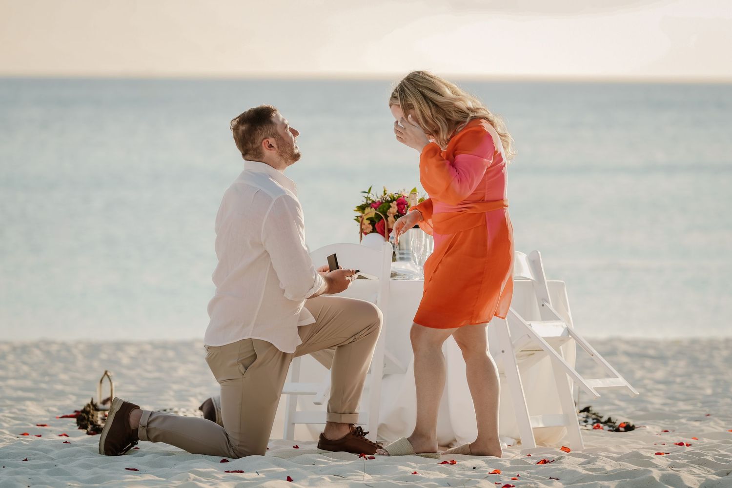 Beach proposal scene with person kneeling in white attire by the ocean.