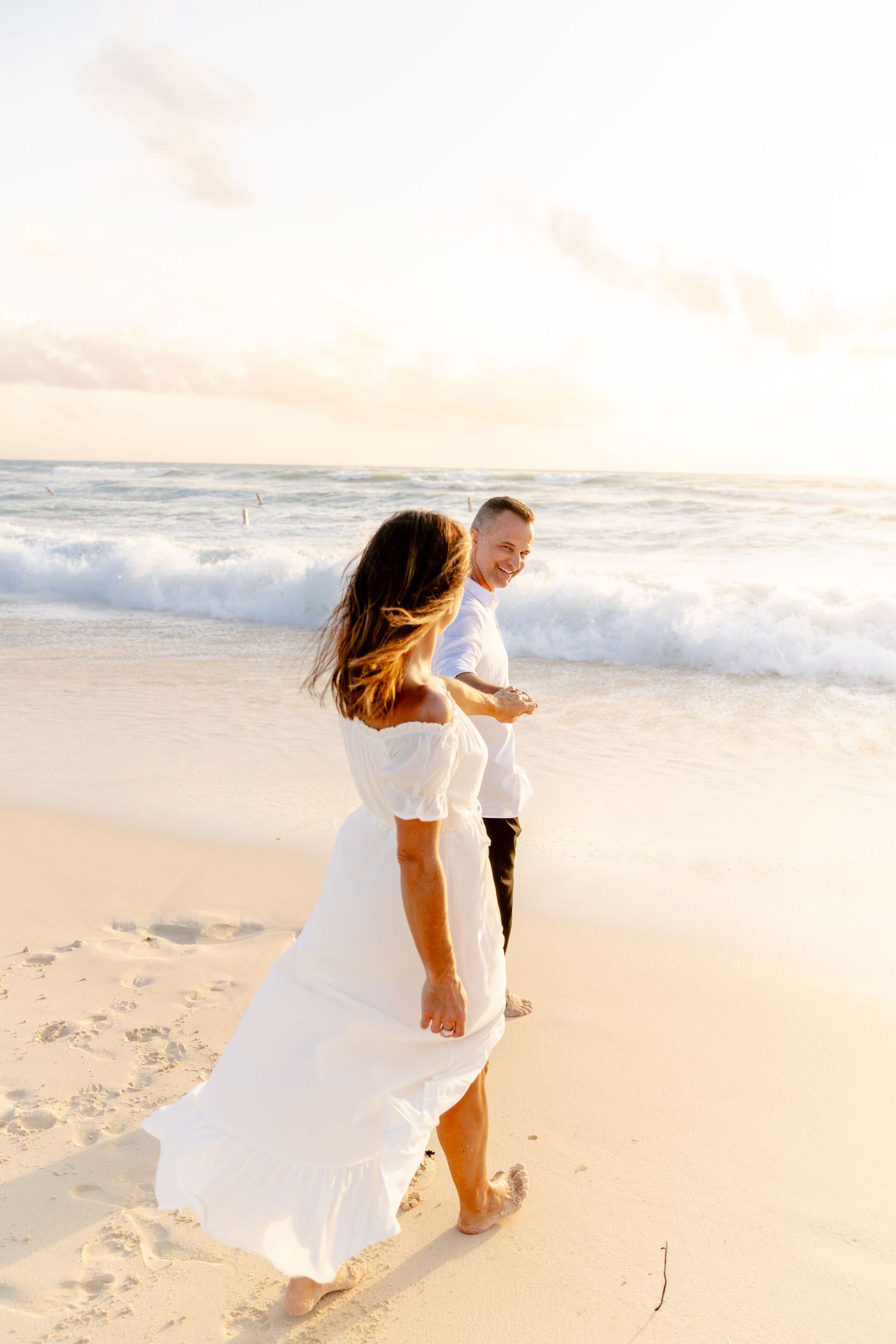 Couple dancing and twirling on beach with flowing white dress catching ocean breeze.