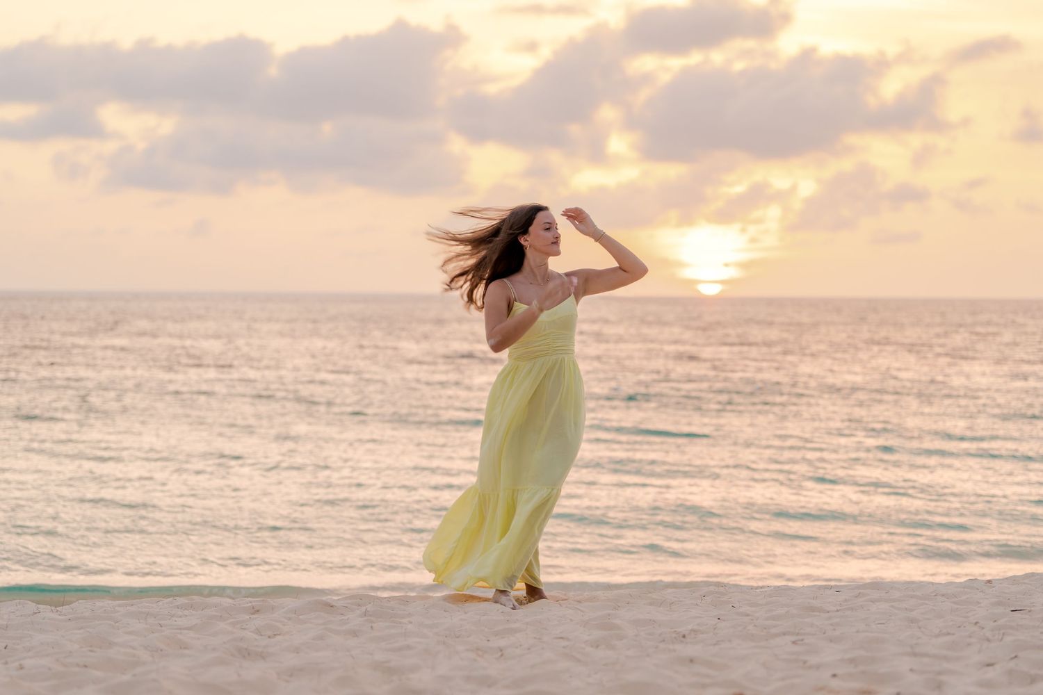 Woman in yellow maxi dress poses on beach during dramatic sunset.