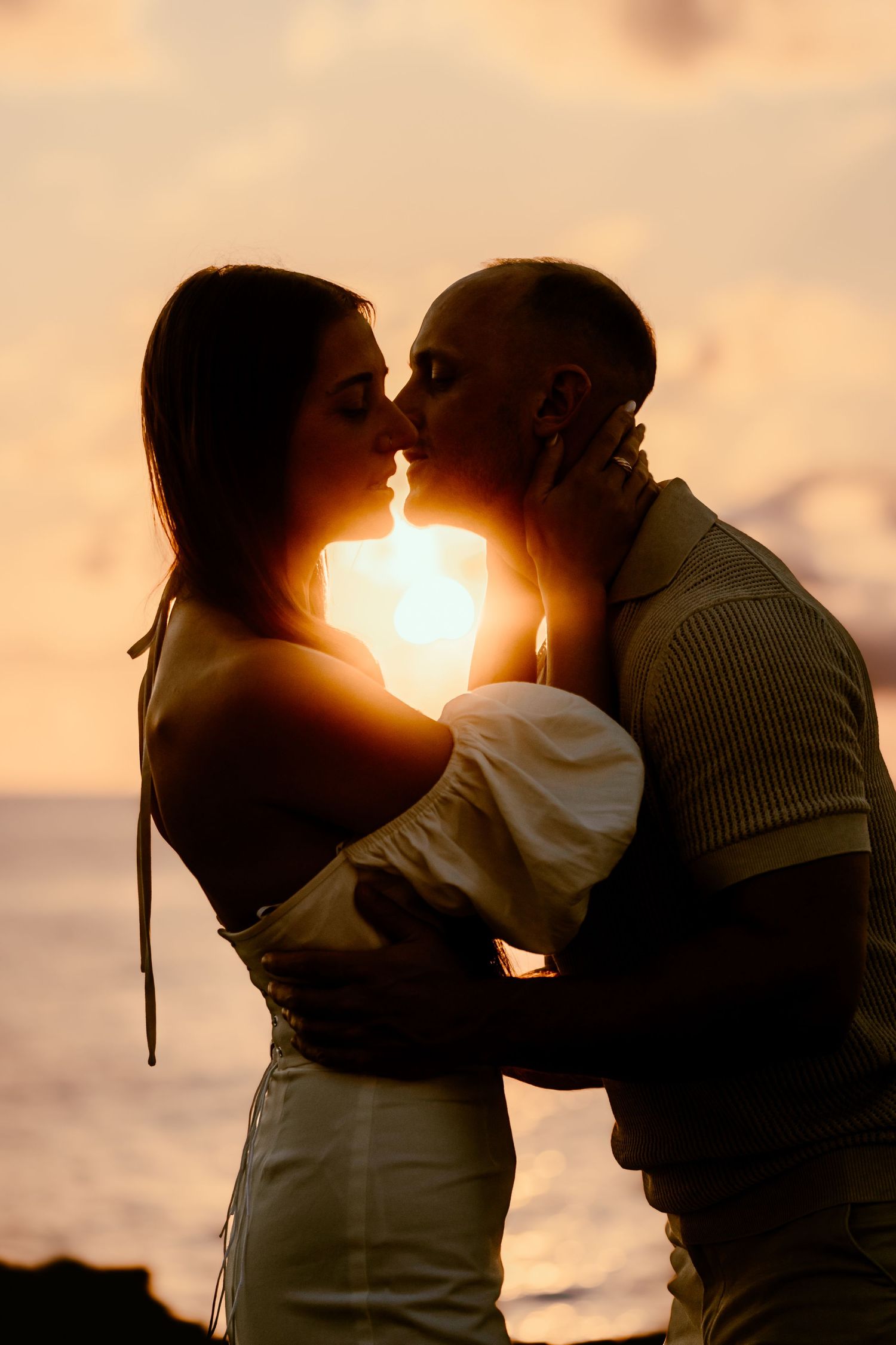 A silhouetted couple embracing with the sun glowing between them during a romantic beach sunset.