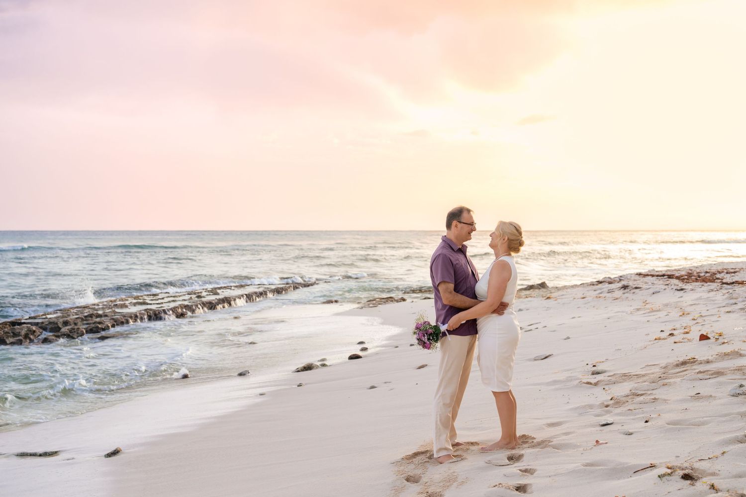 Two people walking hand in hand on a serene beach at sunset.