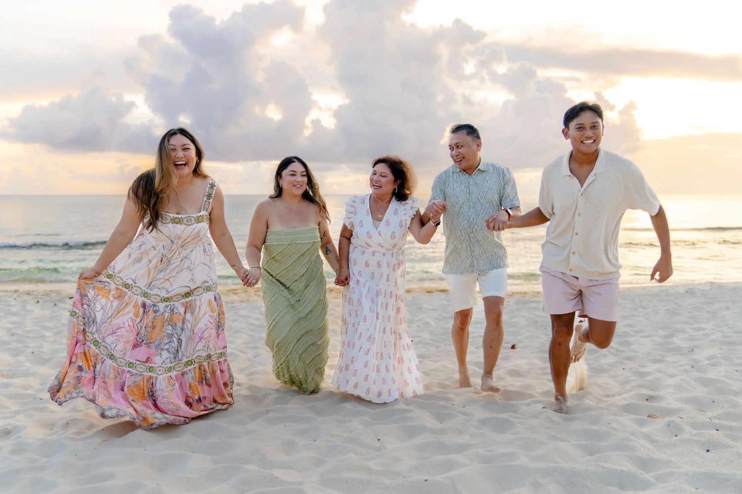 Happy group running and laughing together on beach at sunset wearing coordinated pastel outfits.