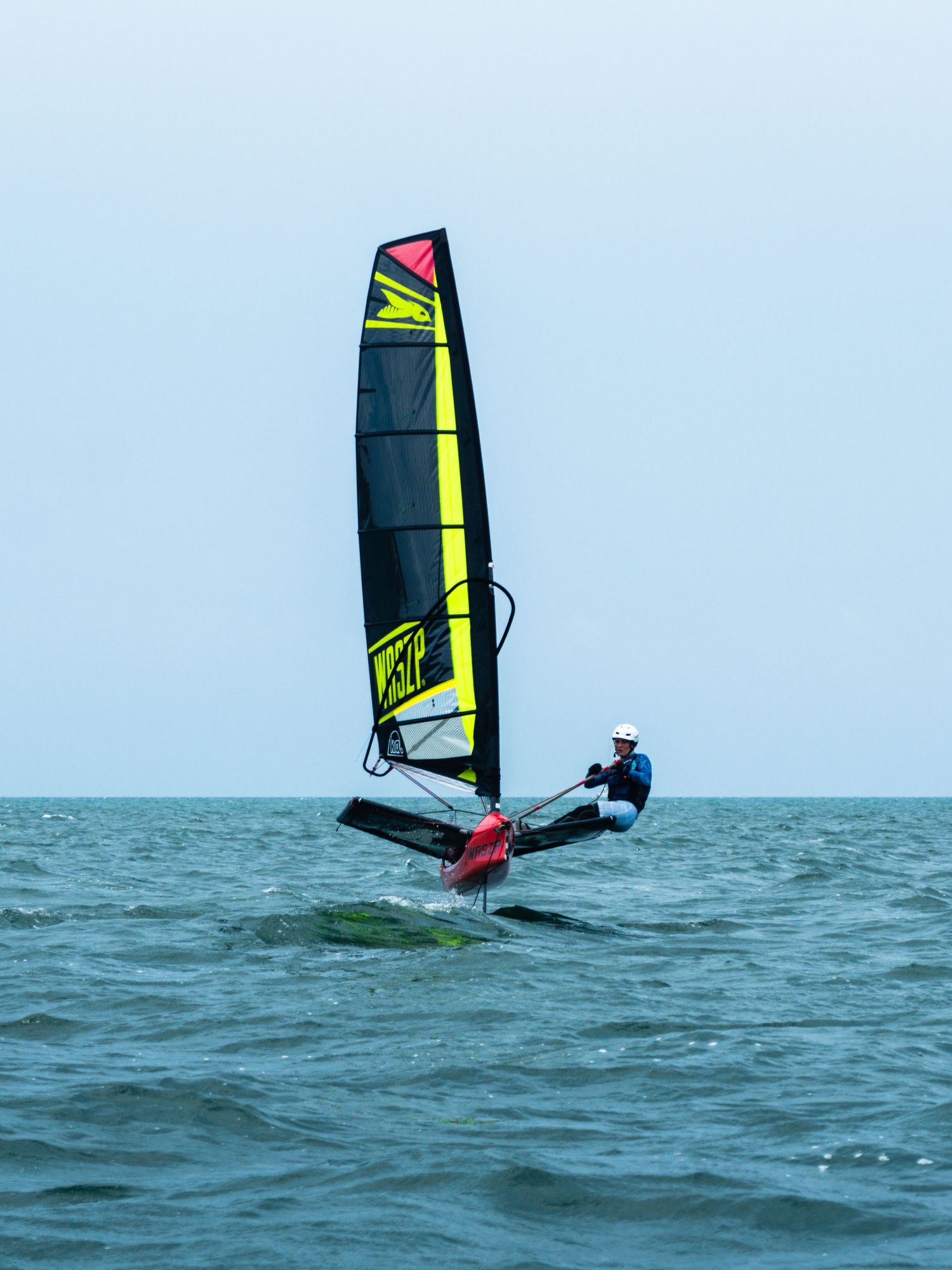Windsurfer on a foiling board with yellow and black sail gliding over blue ocean water.