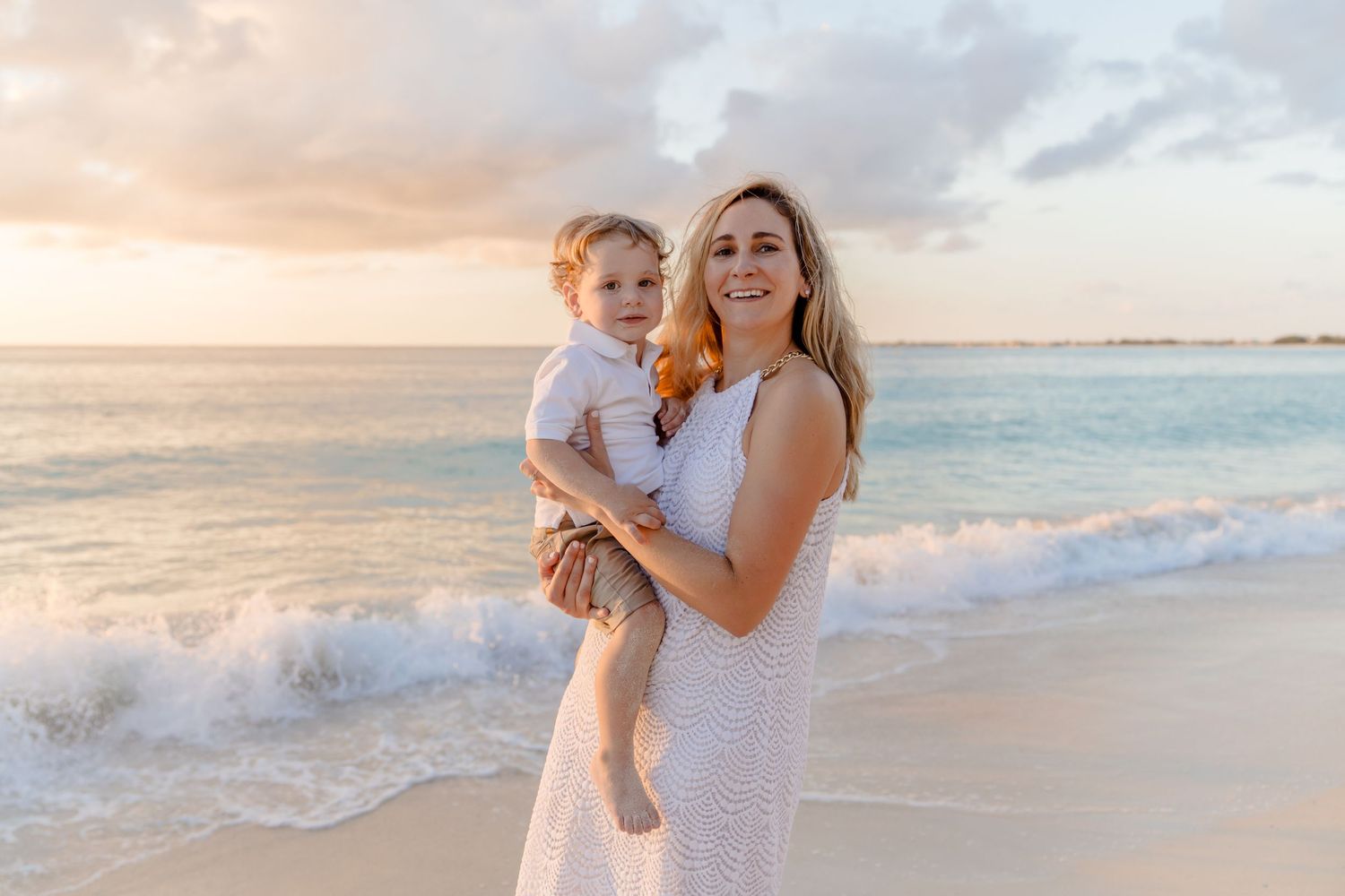 Two figures share a joyful moment on a beach at sunset with gentle waves and warm golden light in the background.