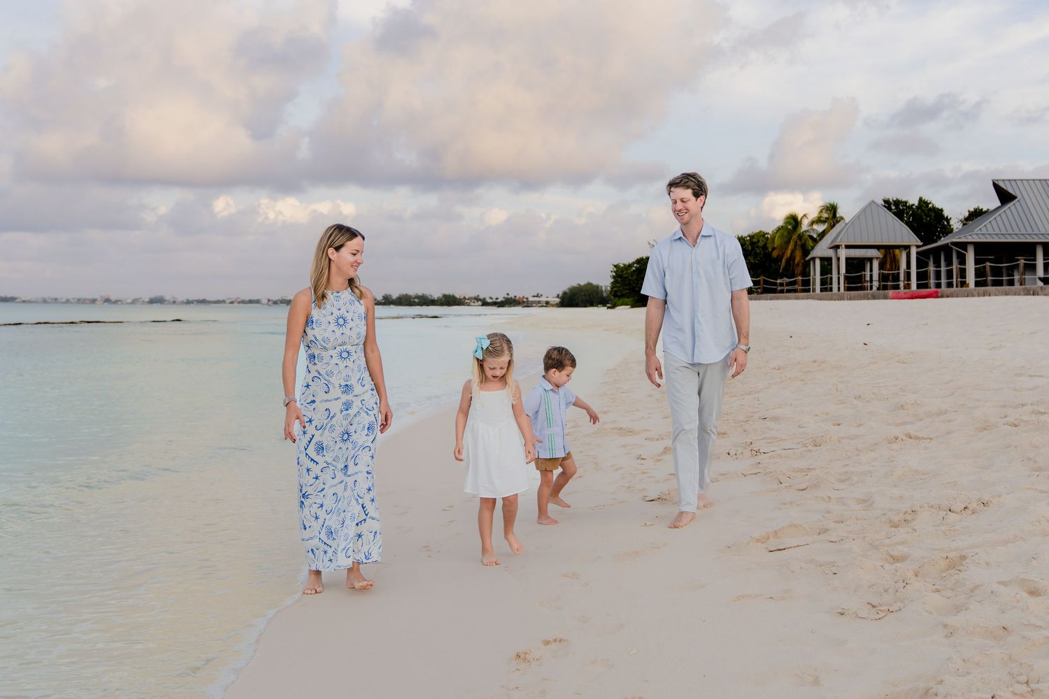 A group walking together on a white sandy beach at sunset with turquoise water and beach houses in the background.