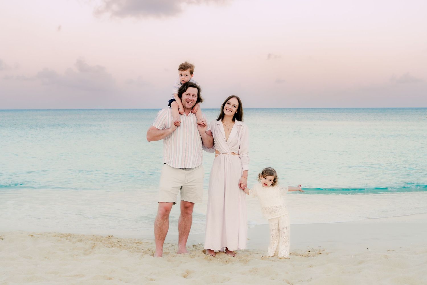 Family plays and laughs together on a pristine beach at sunset with turquoise waters in the background.