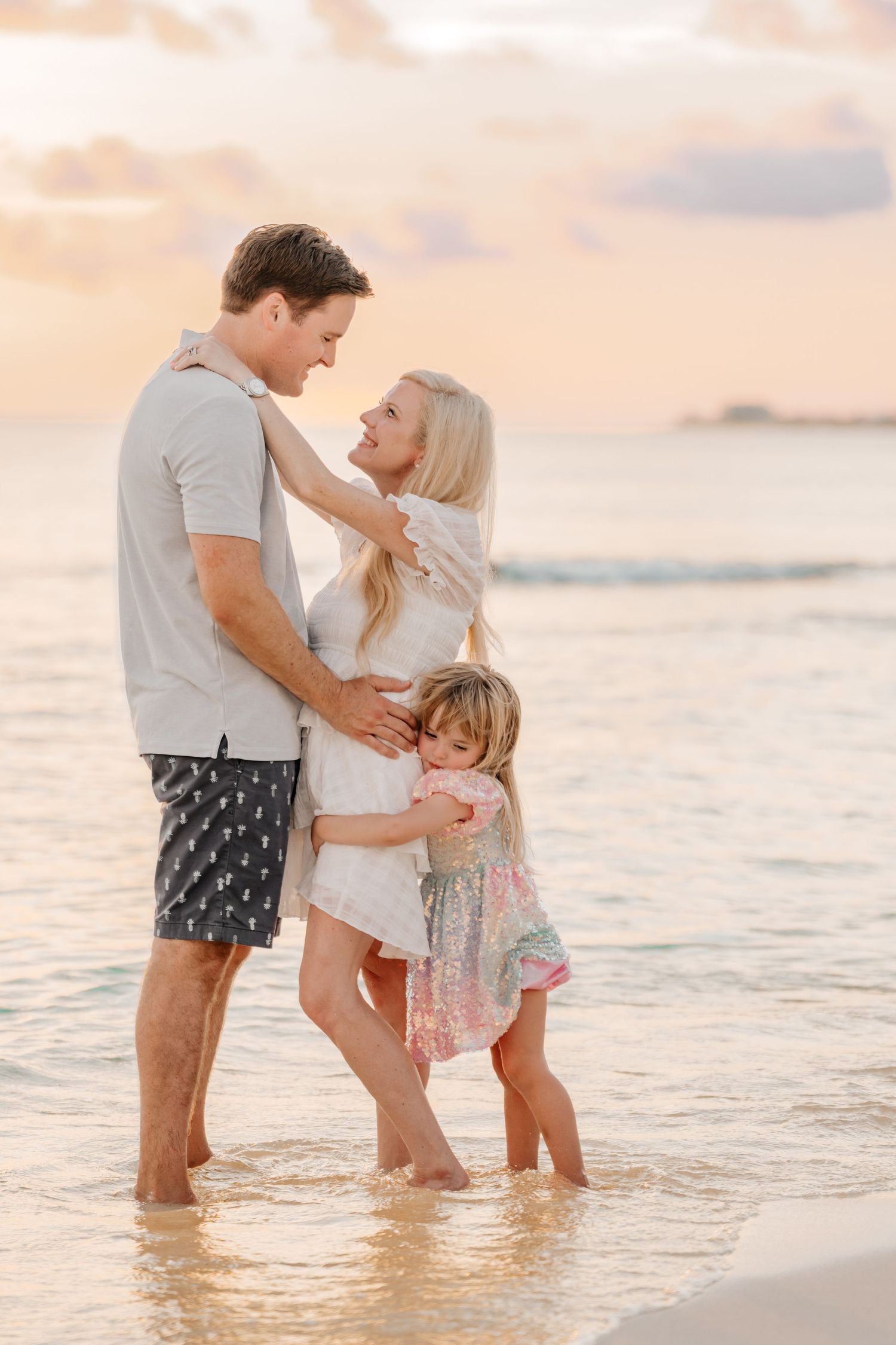 Family playing in shallow ocean waters during sunset with gentle waves.