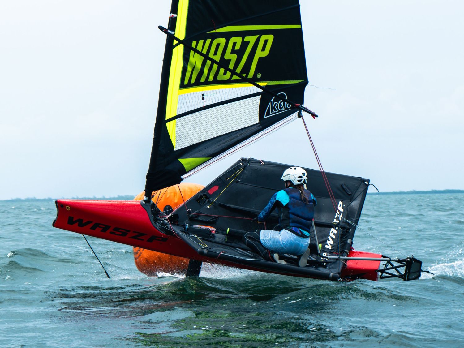 Sailor in a red and white WASZP foiling dinghy heeling sharply on open water.
