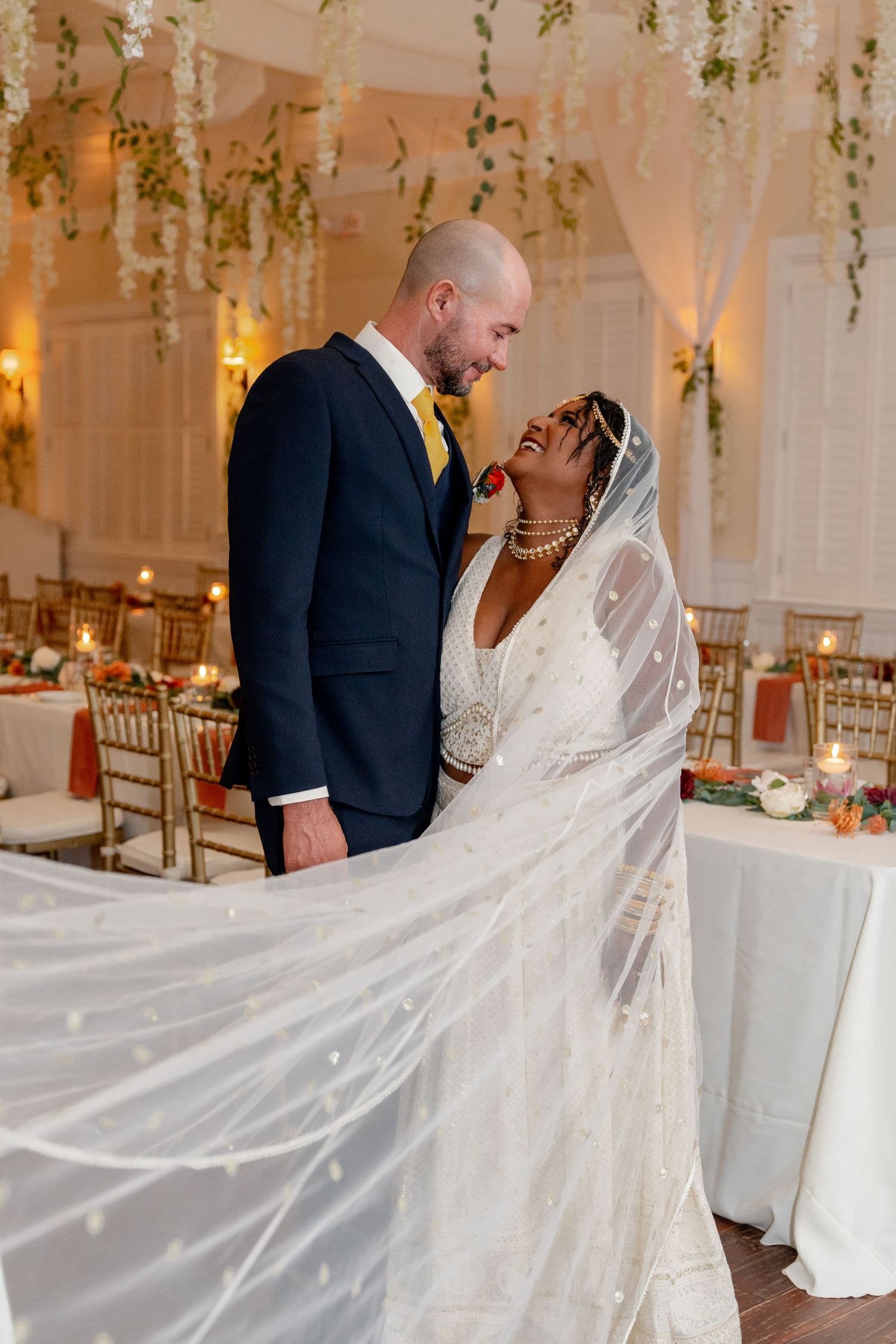 Wedding celebration in white decorated venue with hanging greenery and elegant table settings.