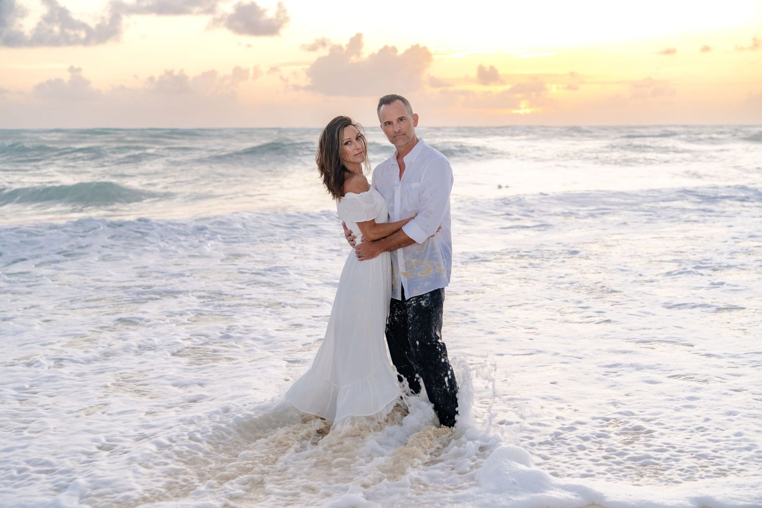 Playful couple gets splashed by ocean waves during beach sunset session.