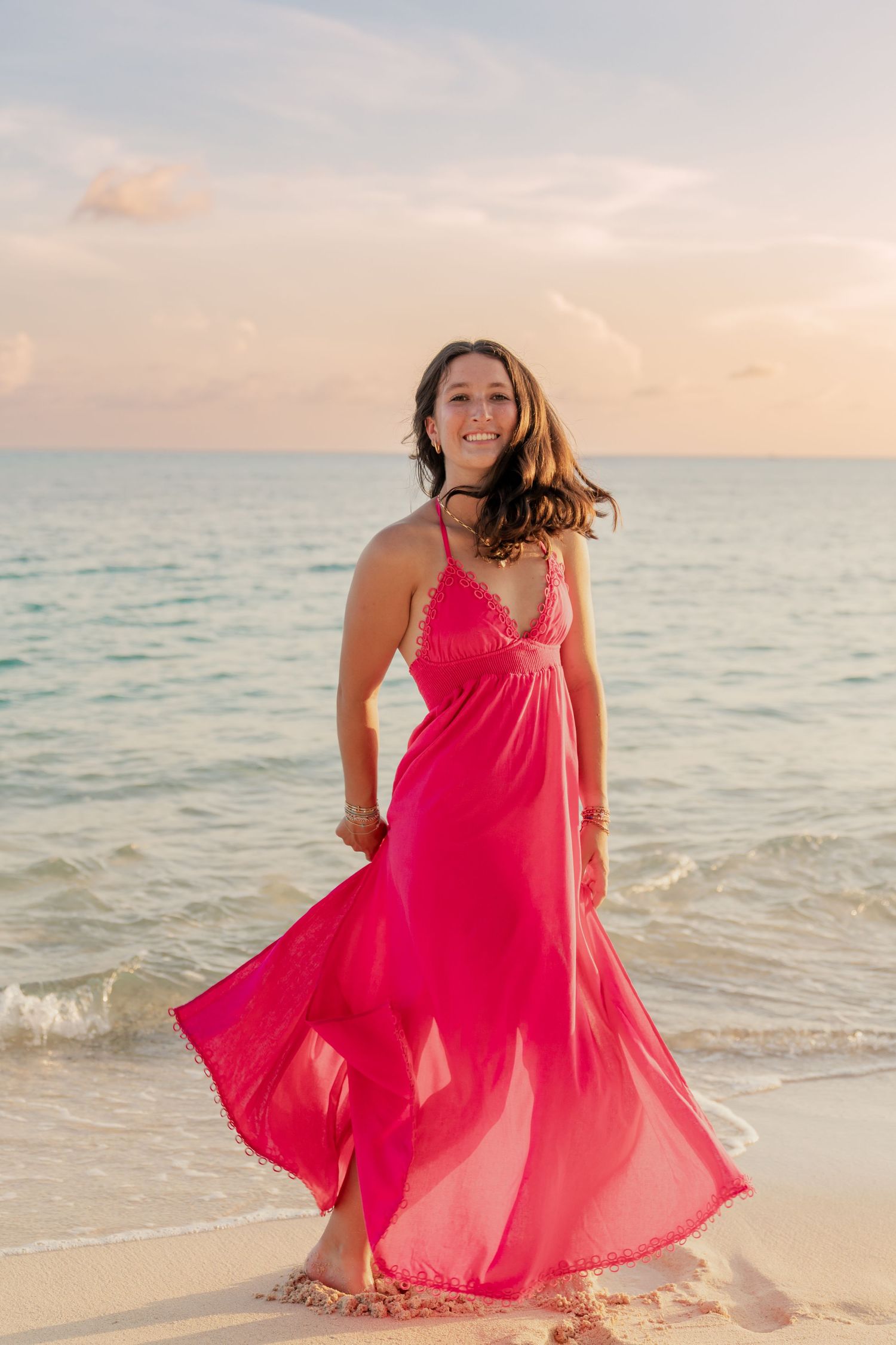 A bright pink dress flows in the ocean breeze as waves lap at sandy shores during golden hour.
