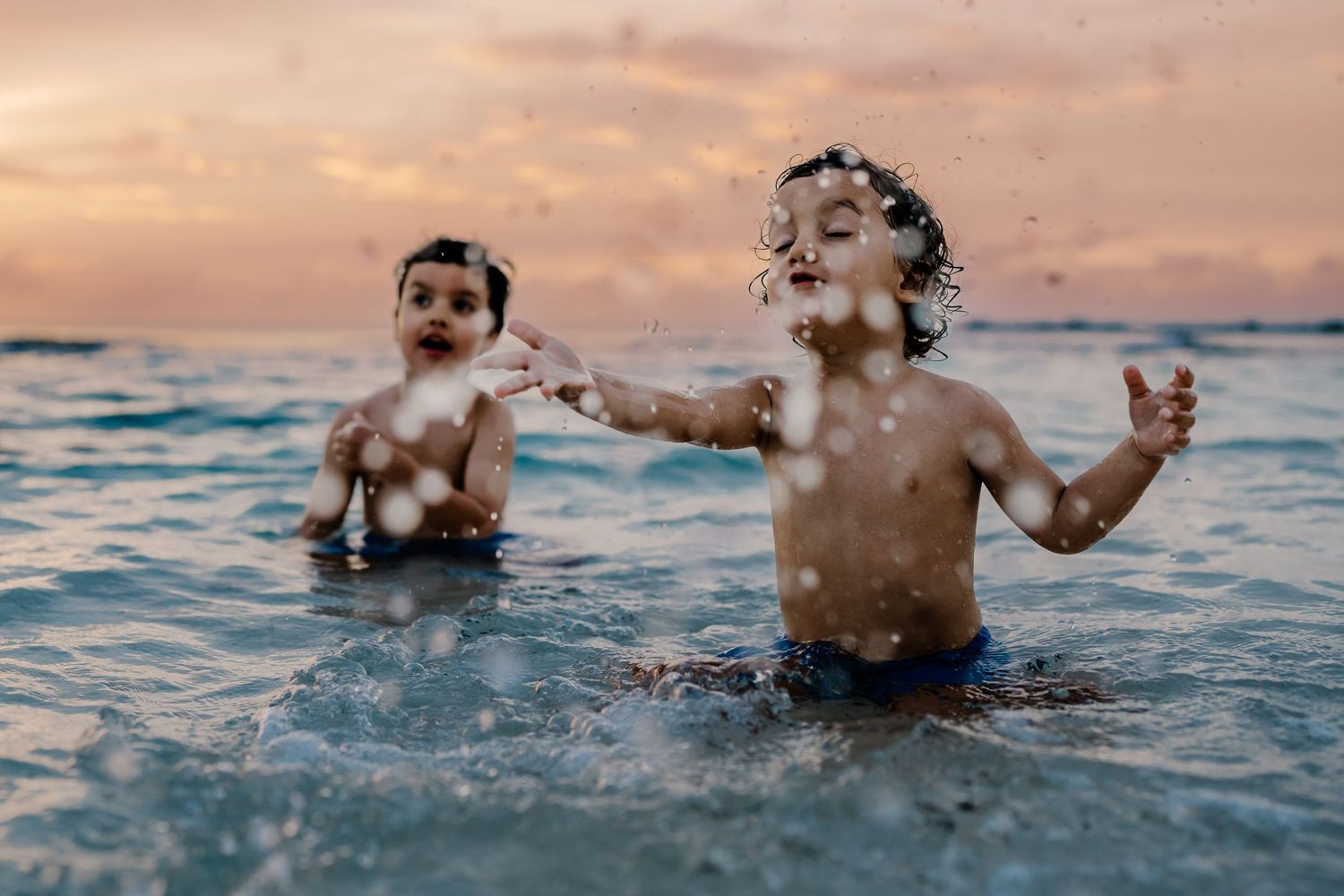 People splashing and playing in the ocean during sunset.