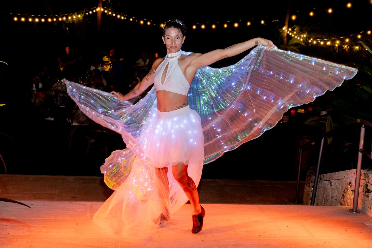 Performer dancing with illuminated costume under string lights at night.