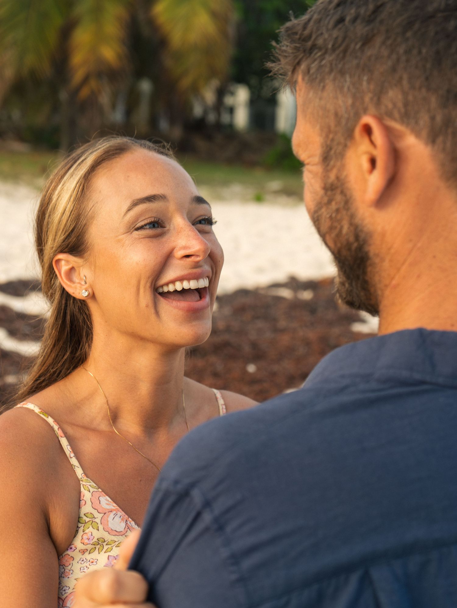 Smiling blonde woman laughing with her partner on a sunny tropical beach.