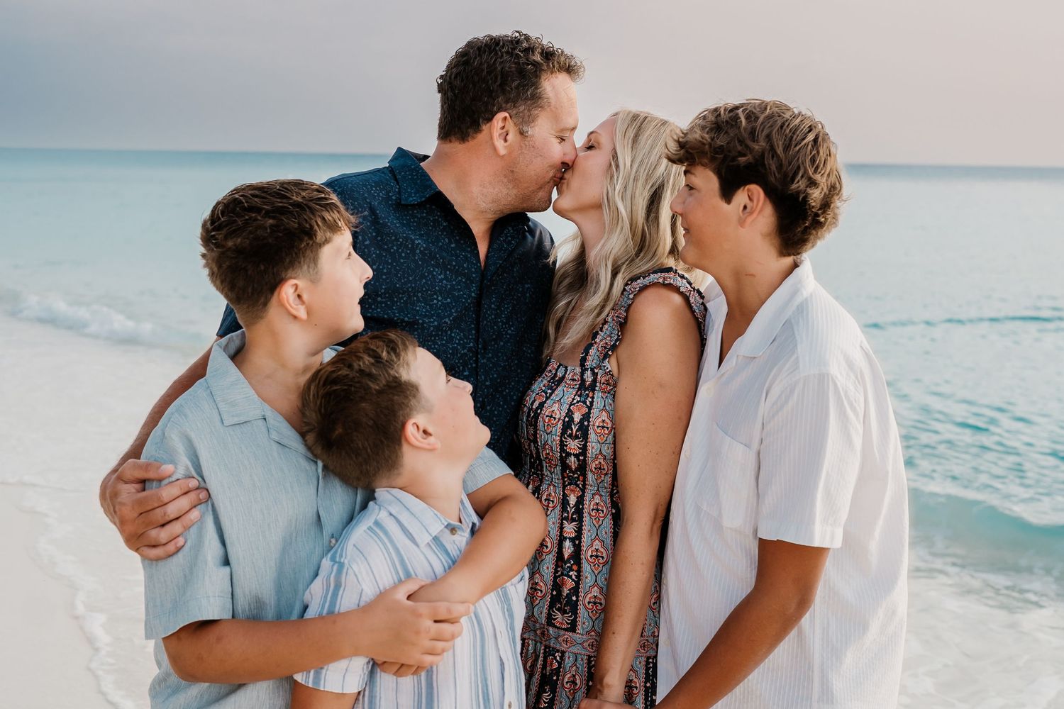 Intimate family embrace on the beach during sunset with ocean waves in background.