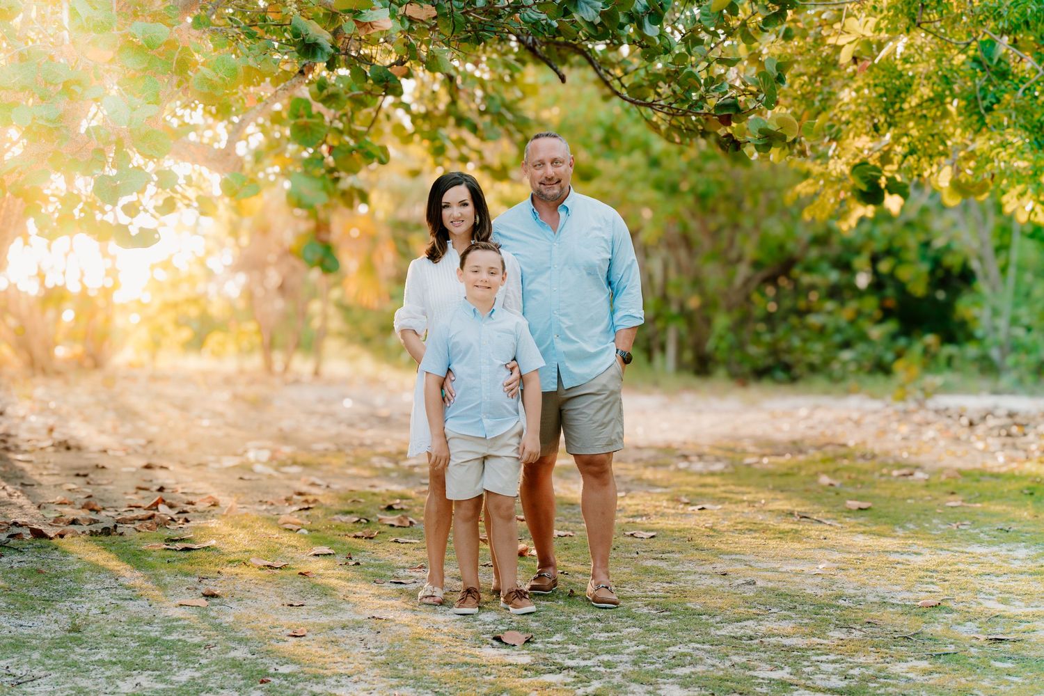 A family poses for outdoor portraits in a sunlit wooded setting during golden hour.