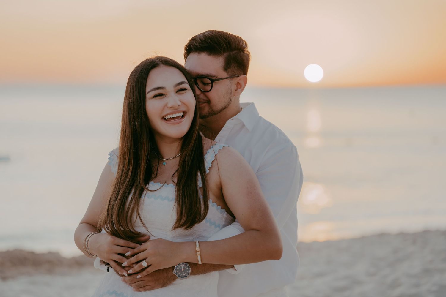 A joyful beach engagement captured during golden hour with the sun setting over the ocean.