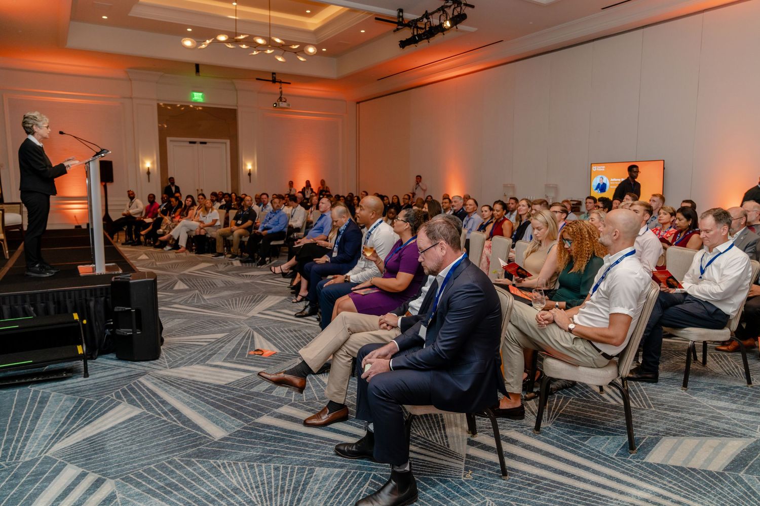 Professional networking event with ambient orange lighting and attendees seated in rows.