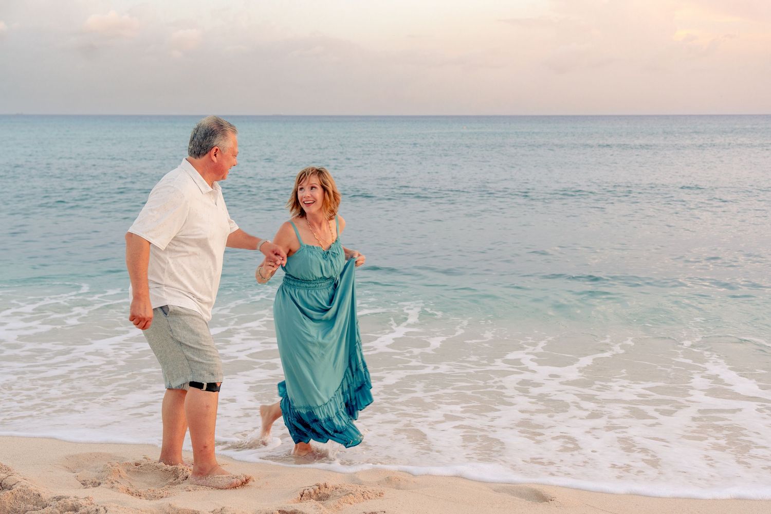 Older couple holding hands and dancing on a tropical beach at sunset, wearing casual summer clothes.