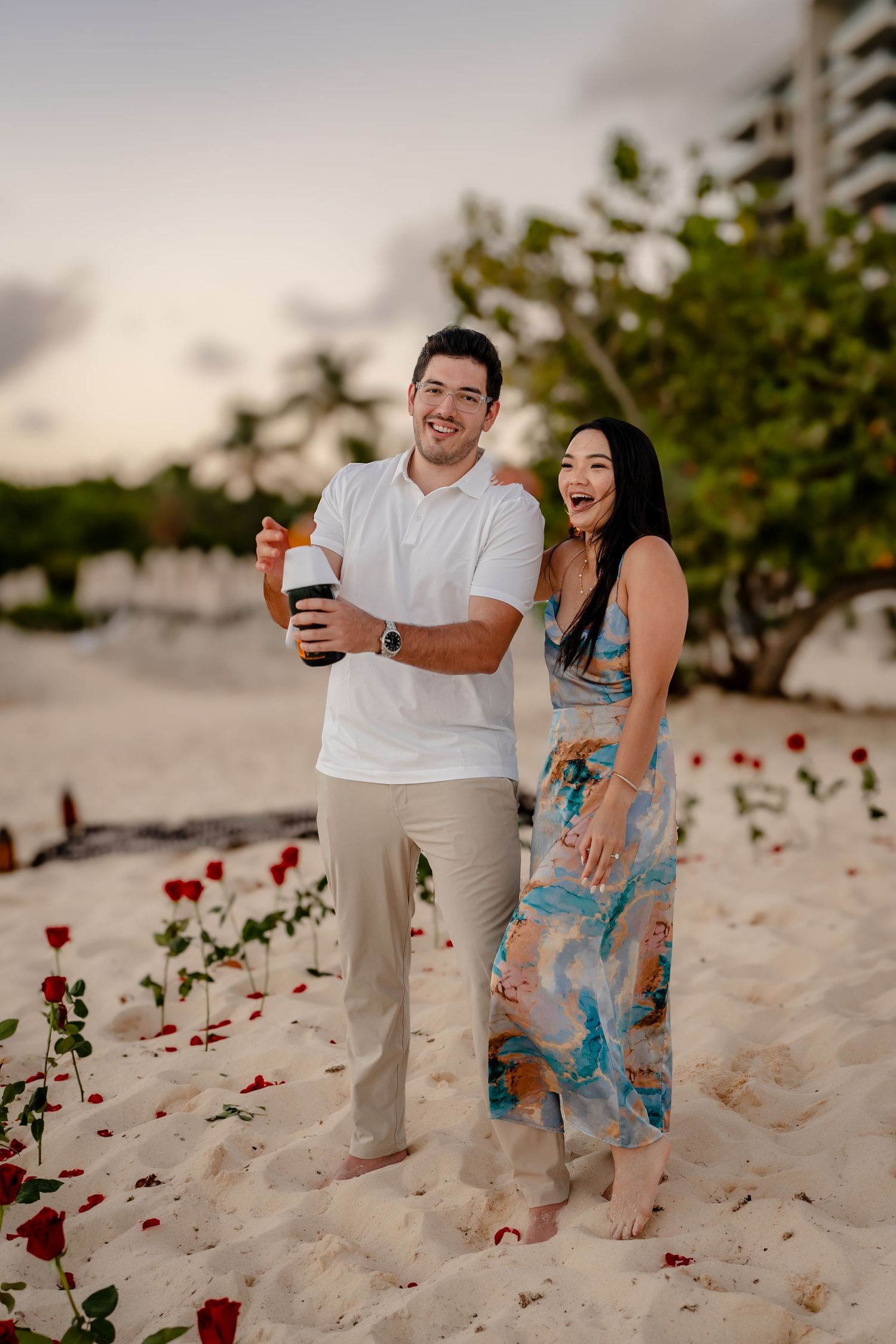 Romantic beach setup with rose petals scattered on sand during golden hour.