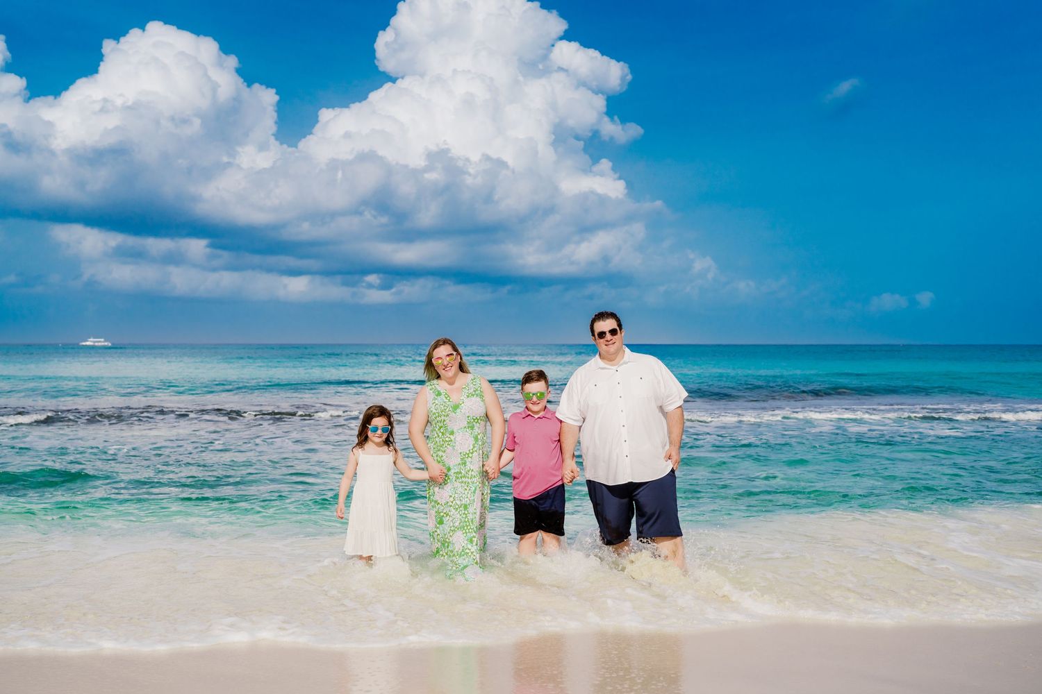 Family beach photoshoot with stunning turquoise ocean and dramatic clouds in background.