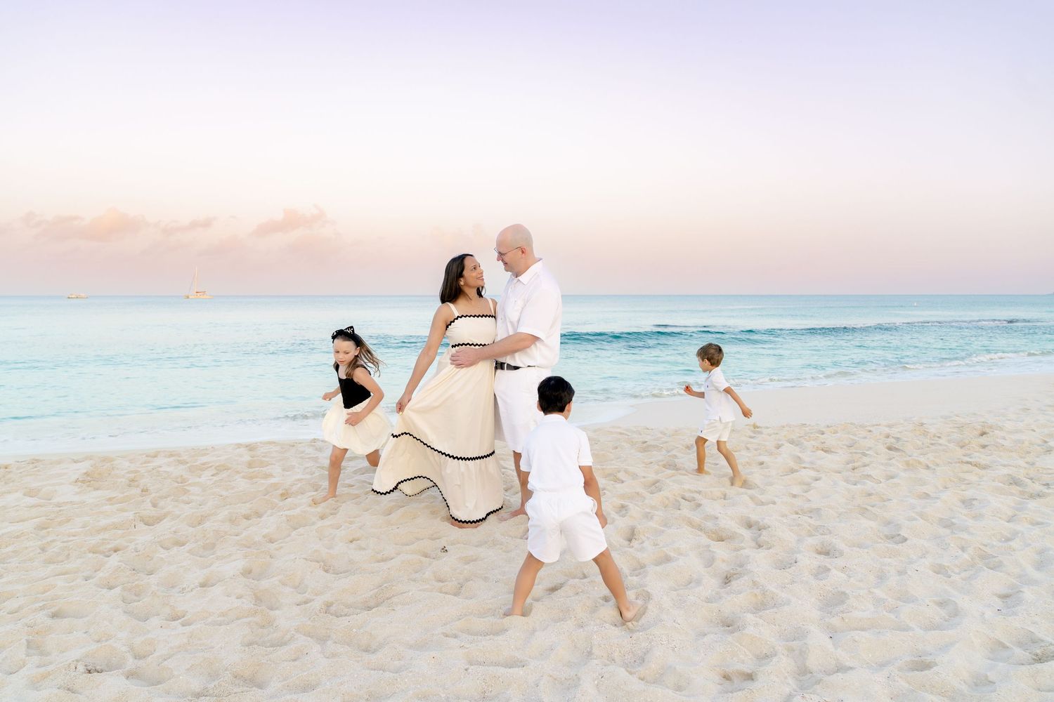 Family playing and running together on beach during sunset with soft pink sky.