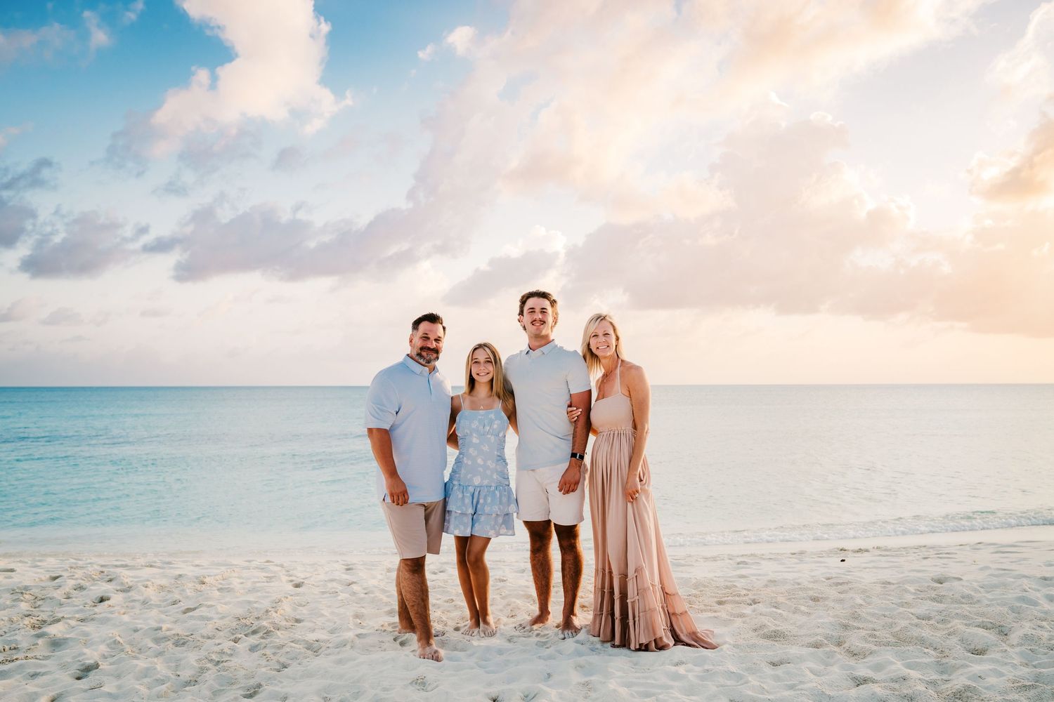 Small group poses together on beach at sunset with pastel sky and calm ocean waters.