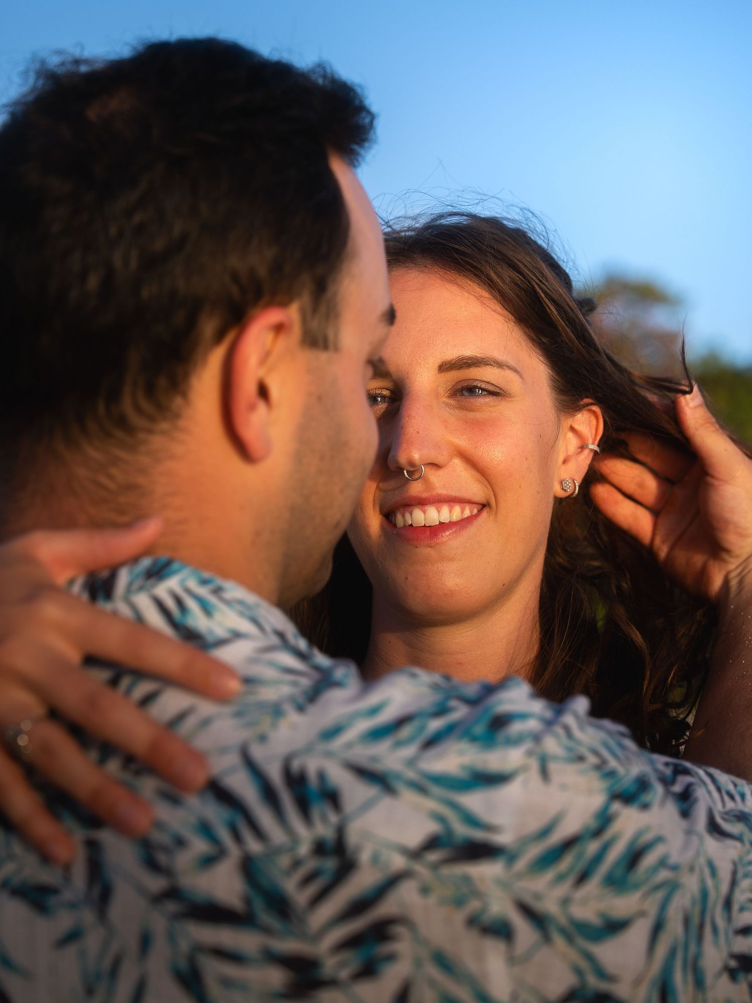 Couple sharing a romantic moment at golden hour, woman smiling as man brushes her hair back.