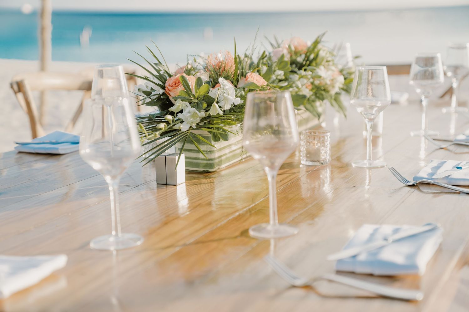 Elegant beach wedding reception table setup with floral centerpieces and glassware.