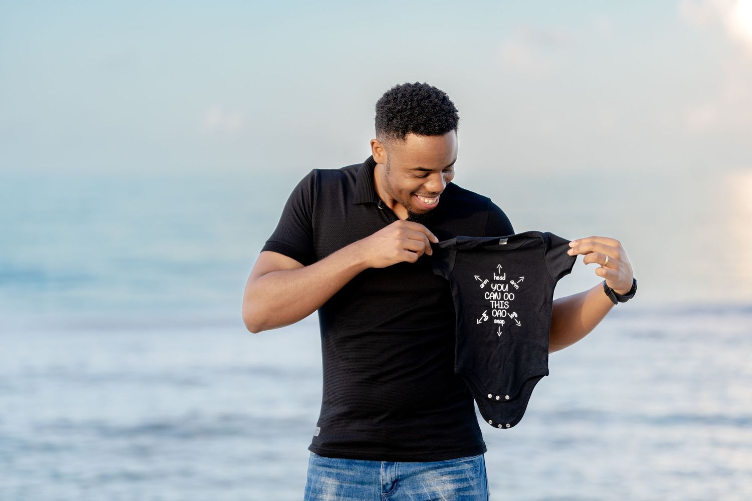 Person holds up tiny black outfit against ocean backdrop during beachside photoshoot.
