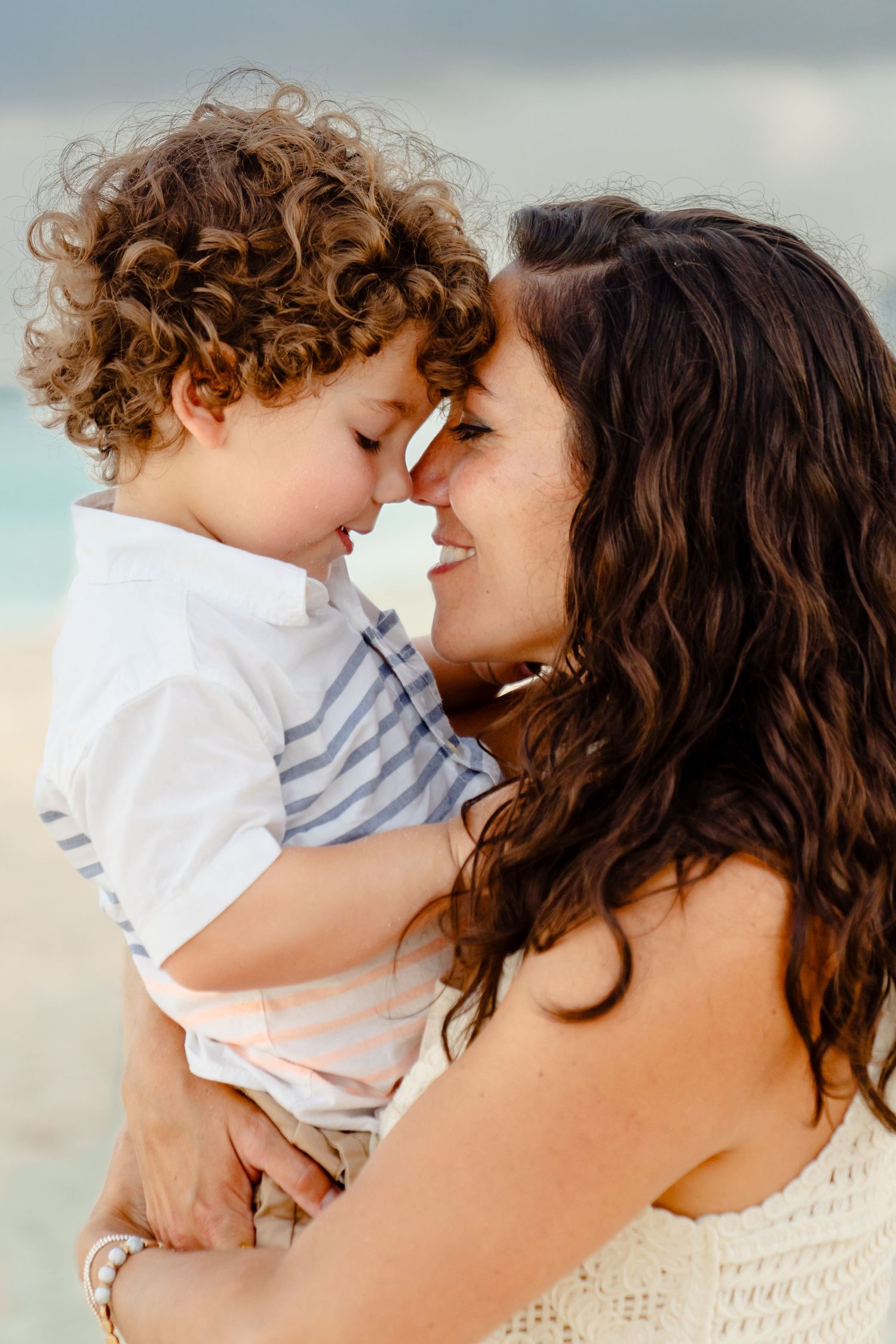 An intimate moment captured between parent and child with curly hair on the beach.