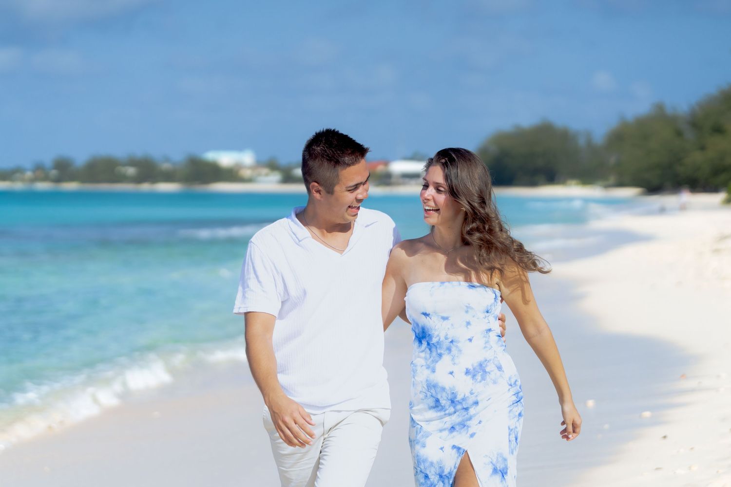 A couple walking together on a tropical beach with turquoise waters and white sand.