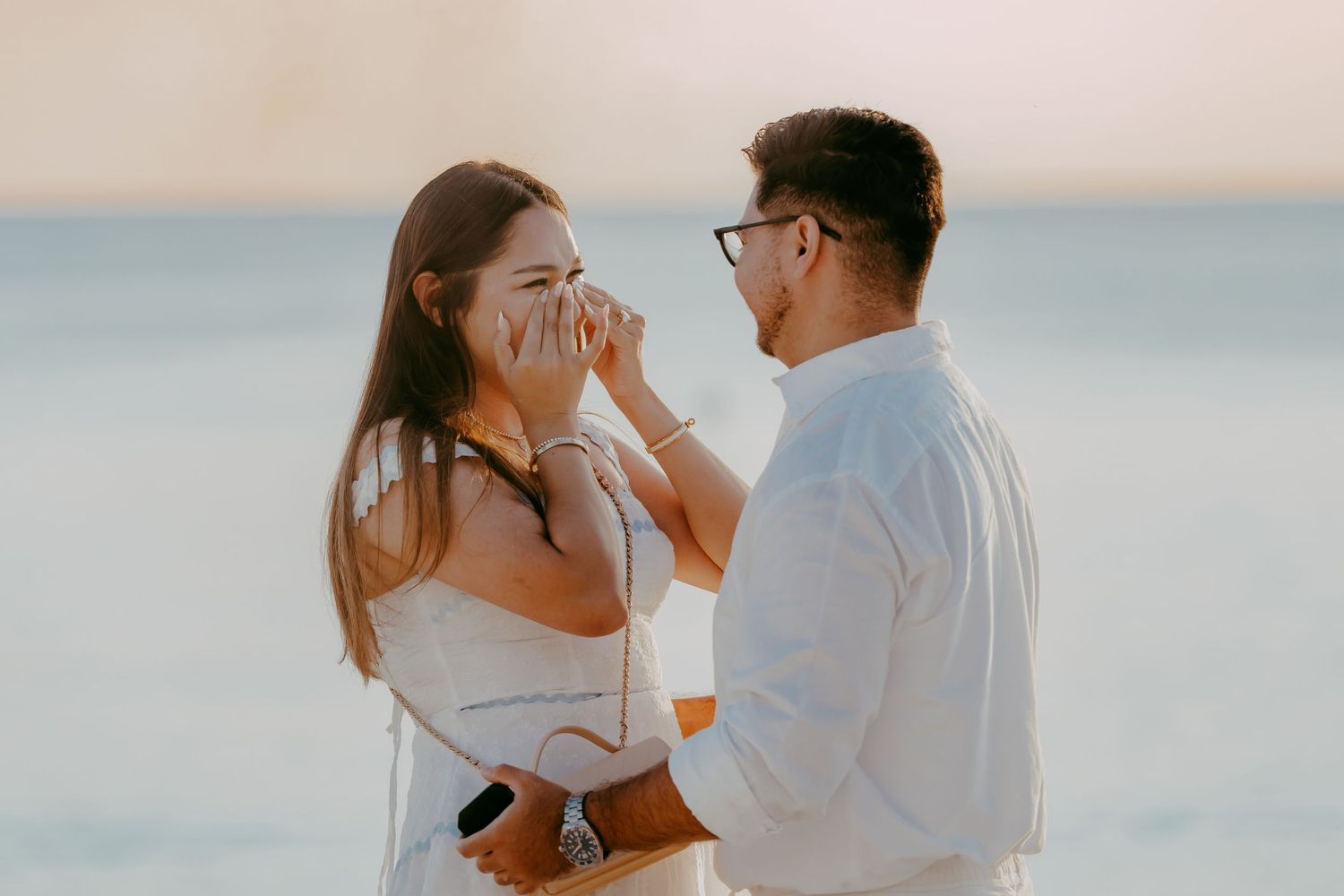 A romantic beach proposal scene with two people in white outfits against an ocean backdrop.