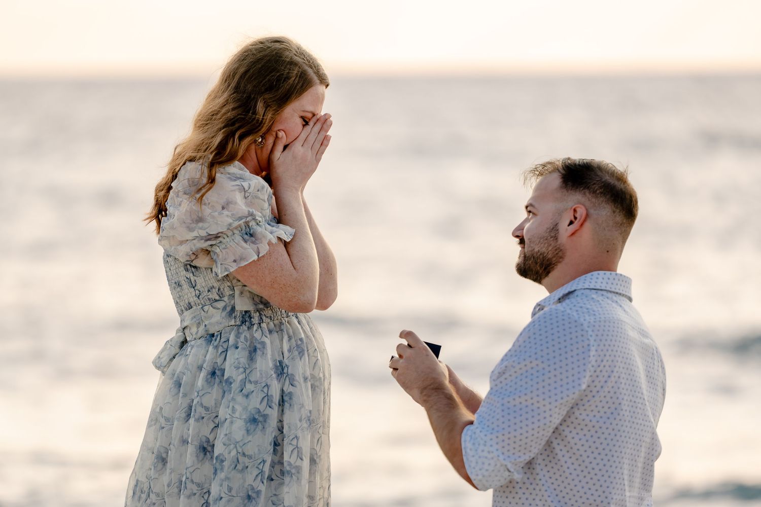 A surprise proposal moment captured at sunset by the ocean.