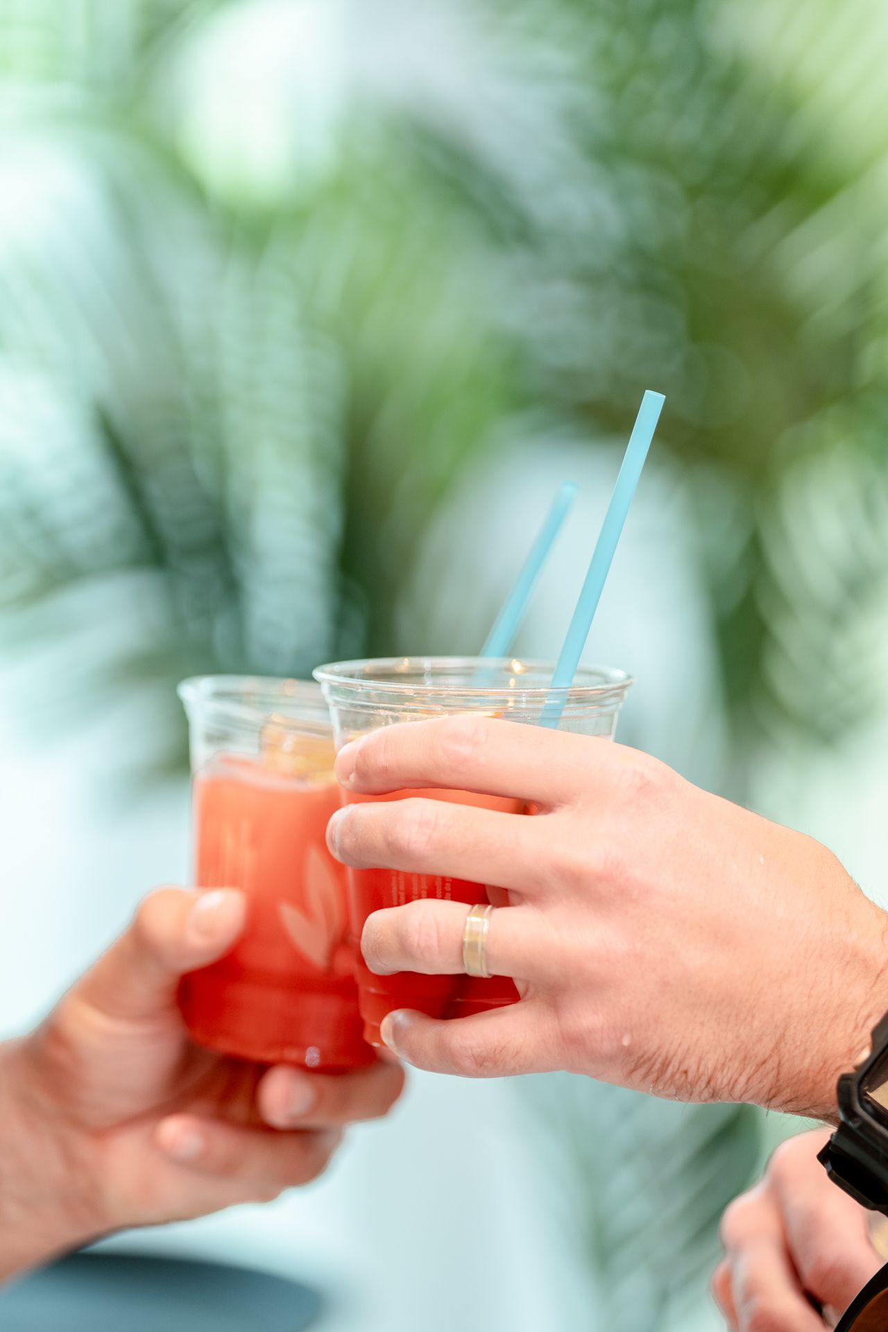 Hands toasting with tropical cocktails garnished with straws against a blurred green background.