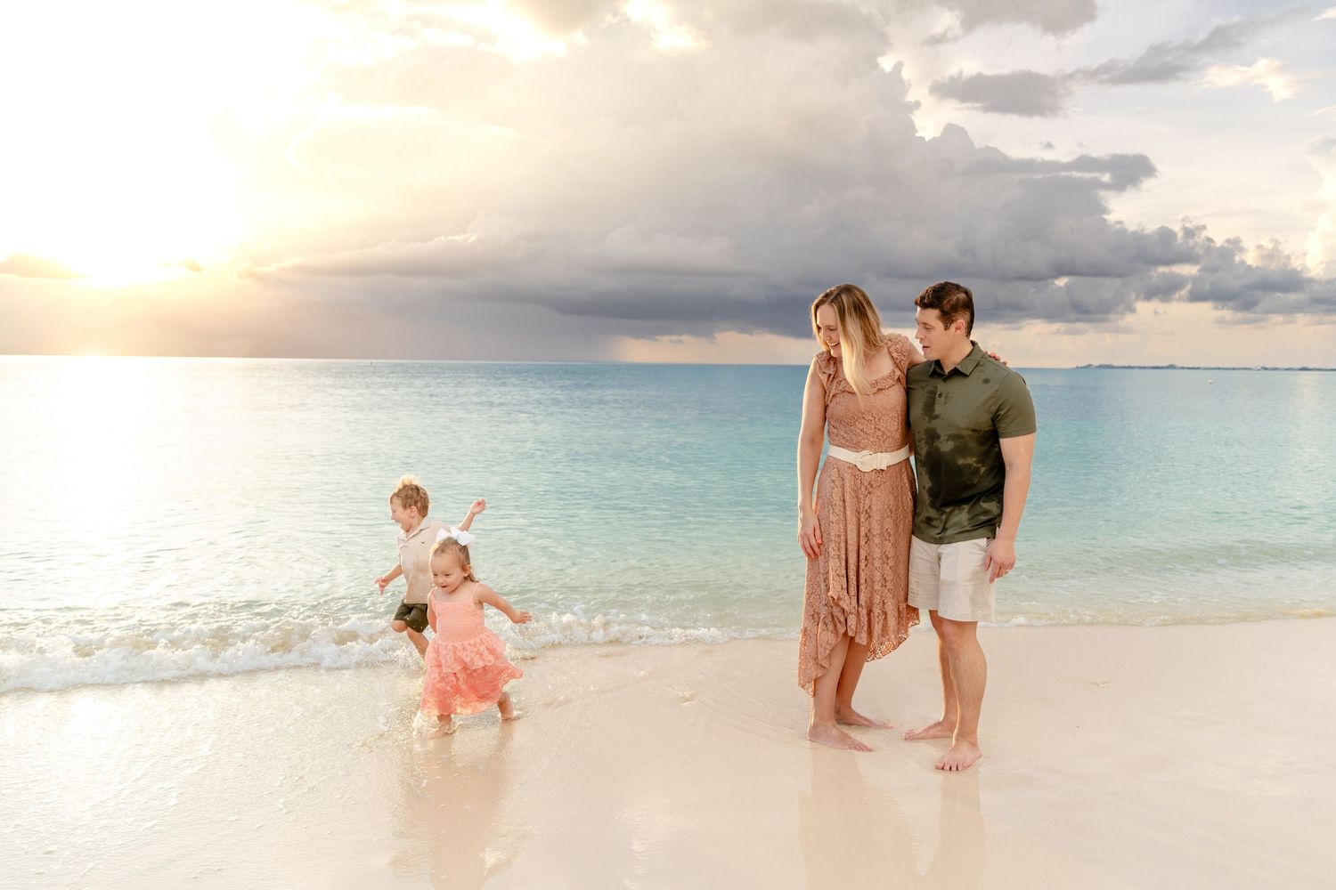 Family enjoying a serene moment on white sand beach during golden hour with dramatic clouds overhead.