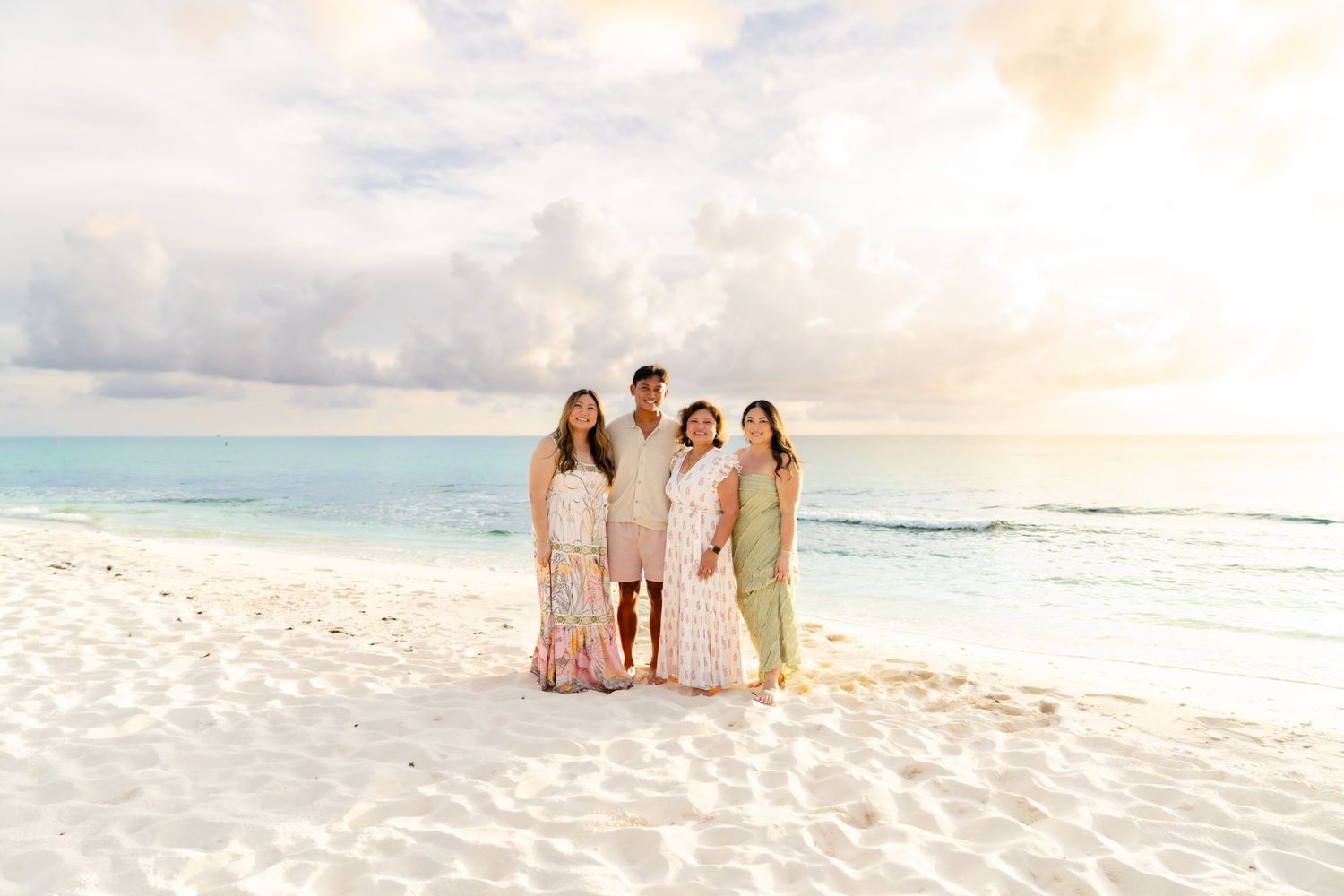 Group portrait on a white sandy beach with gentle waves and sunset sky in the background.