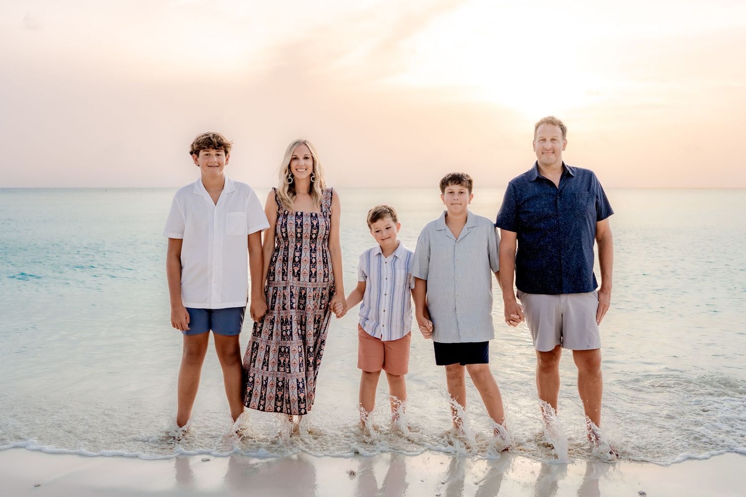 Group portrait of a family lined up along the shoreline during sunset at the beach.