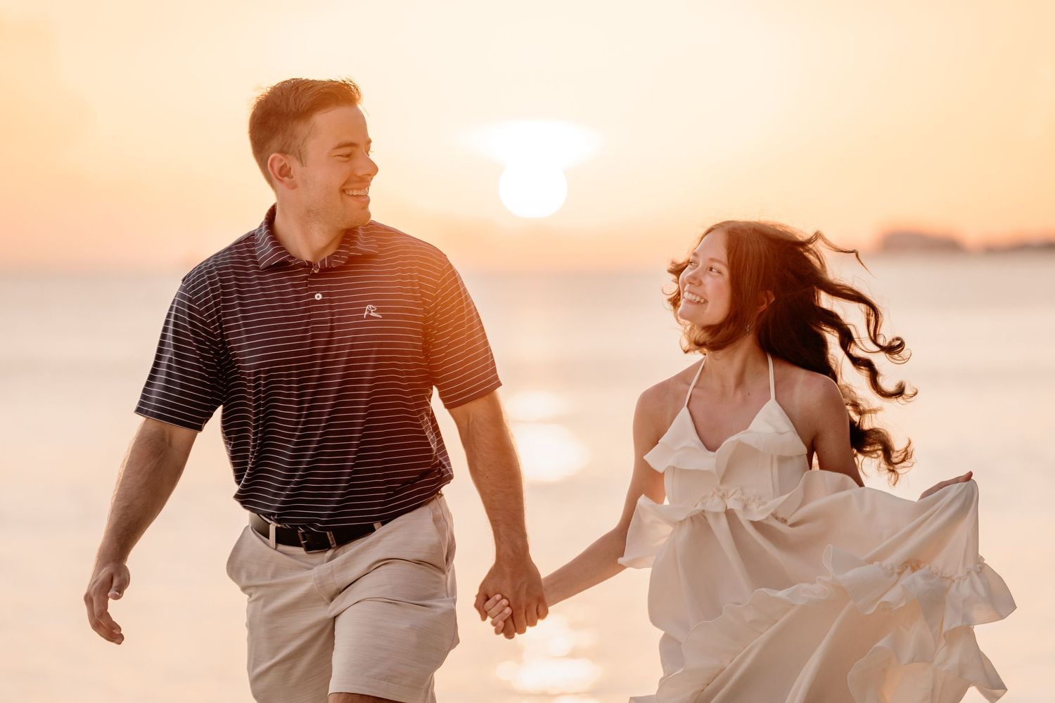 Playful beach engagement session with couple running through golden sunlight.
