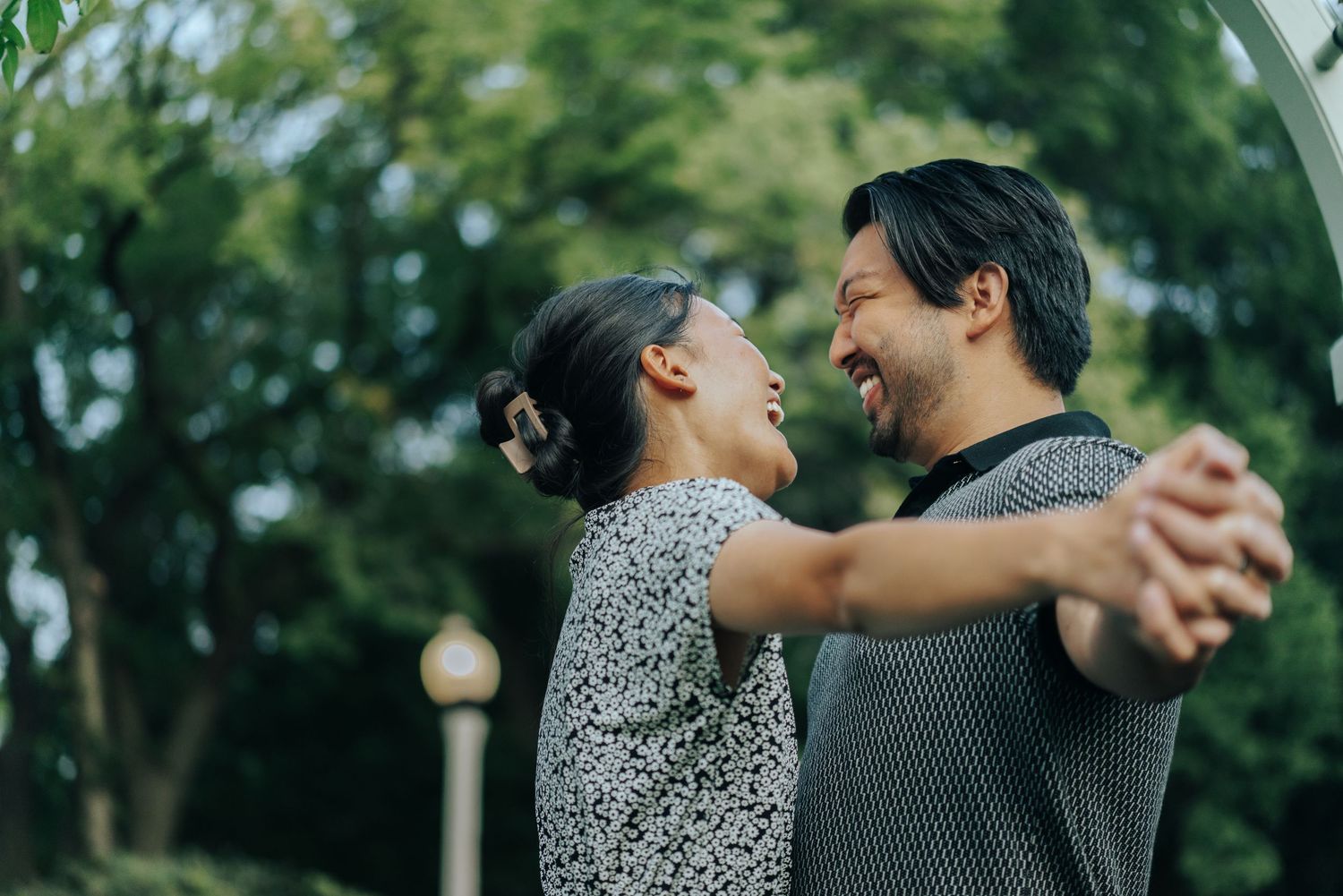 A joyful couple dances together outdoors, smiling and holding hands in a lush green park setting.