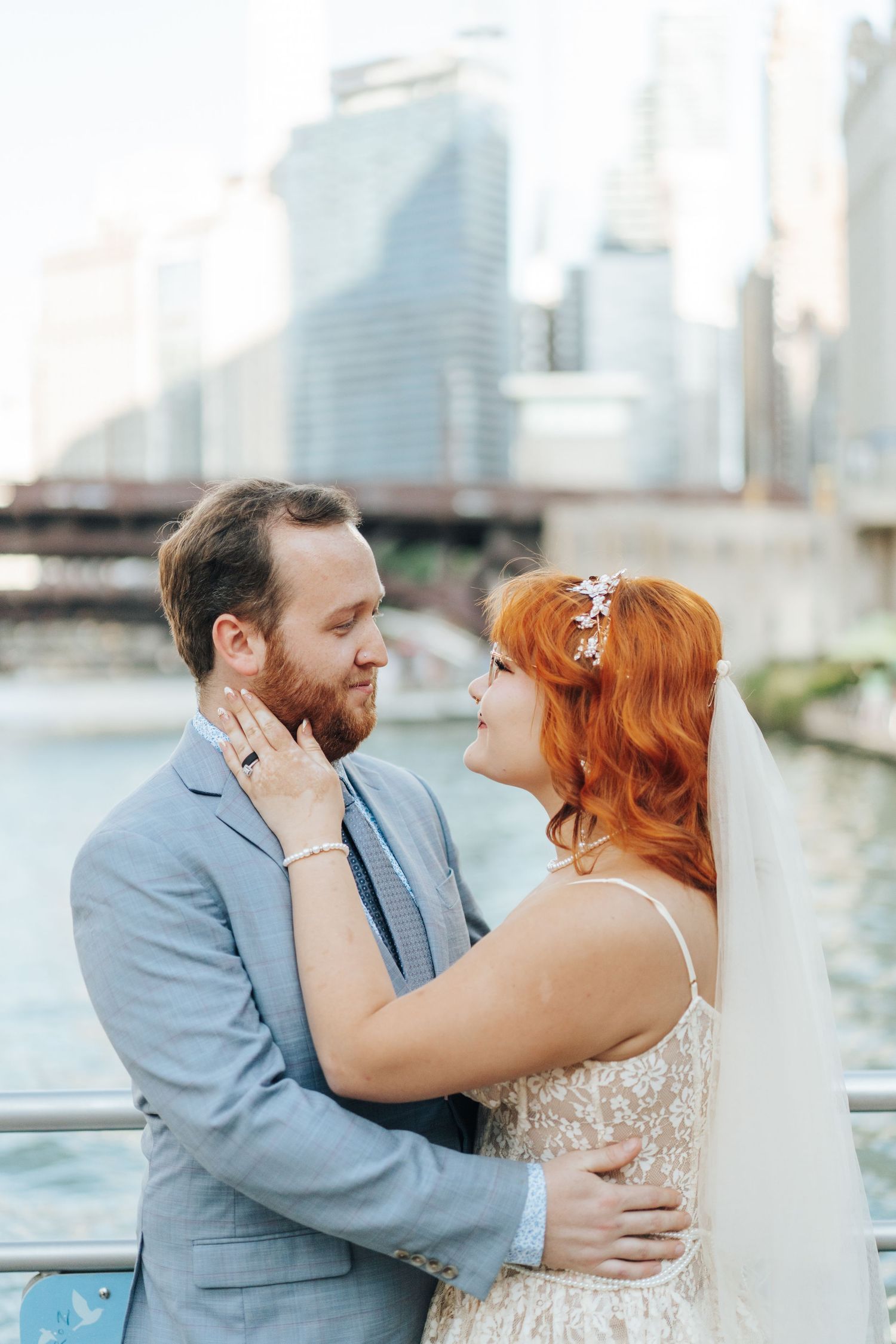 A bride and groom embrace romantically on a waterfront with Chicago city skyline in the background on their wedding day.