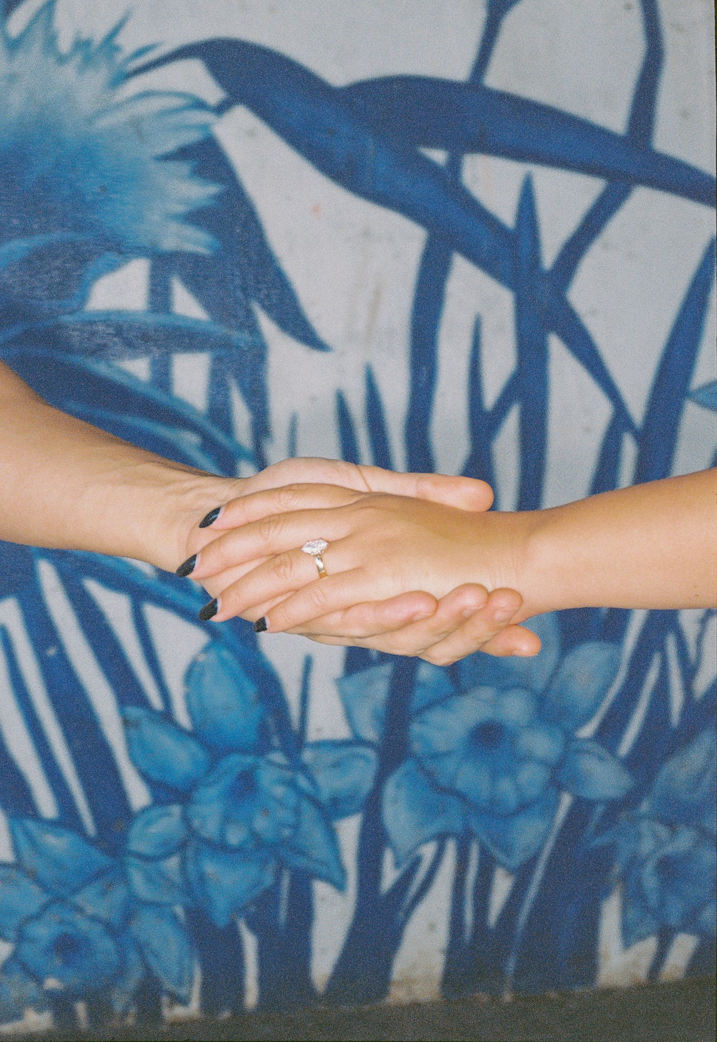 Delicate hand holding connection showcasing ring against blue mural.
