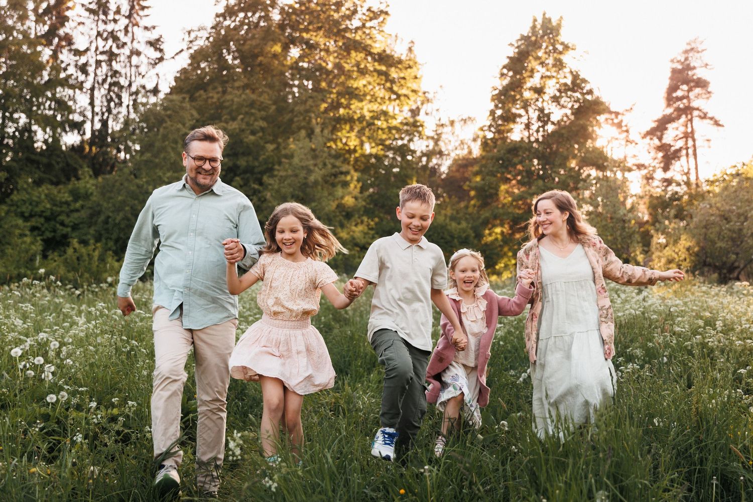 Happy family with three children running through a sunny wildflower meadow at golden hour.