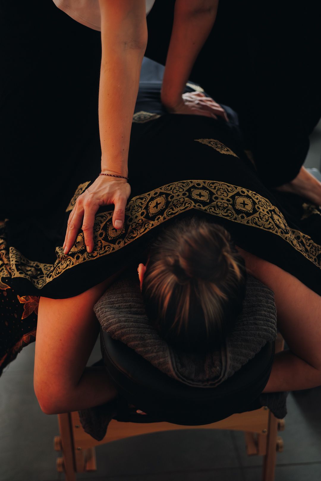 Massage therapist performing a back massage on a client lying face down on a massage chair.