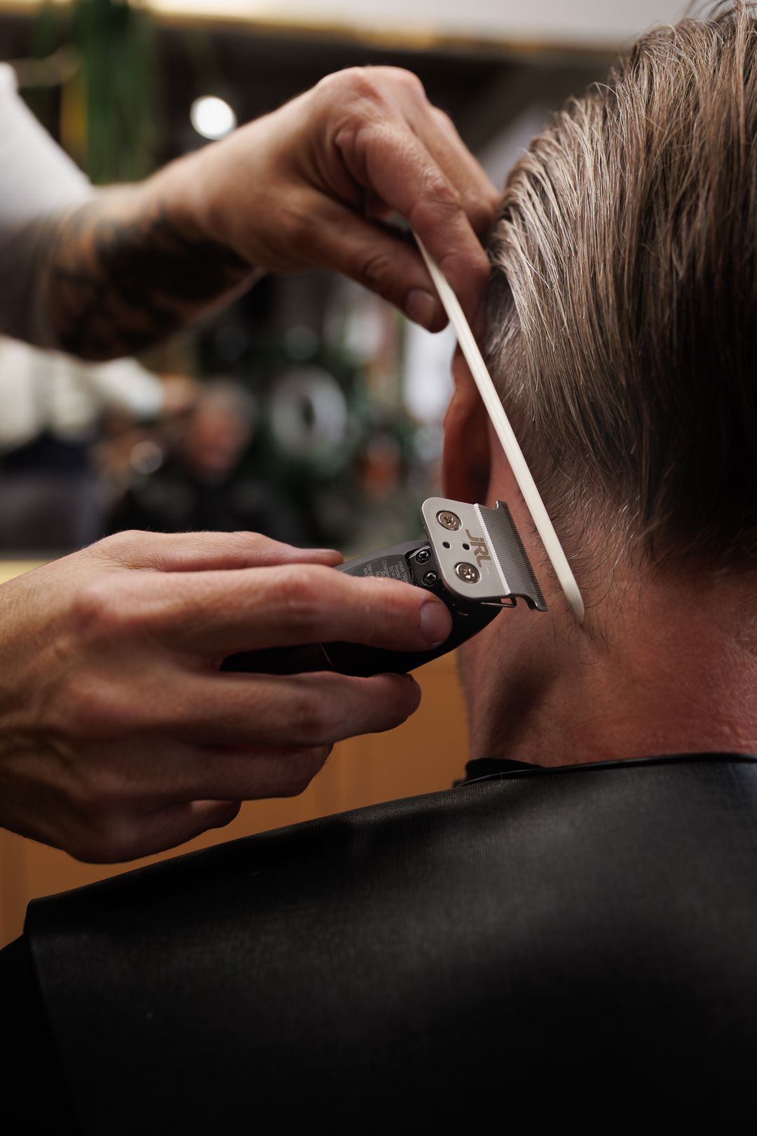 Barber using electric clippers and comb to trim the back of a man's hair in a professional barbershop.