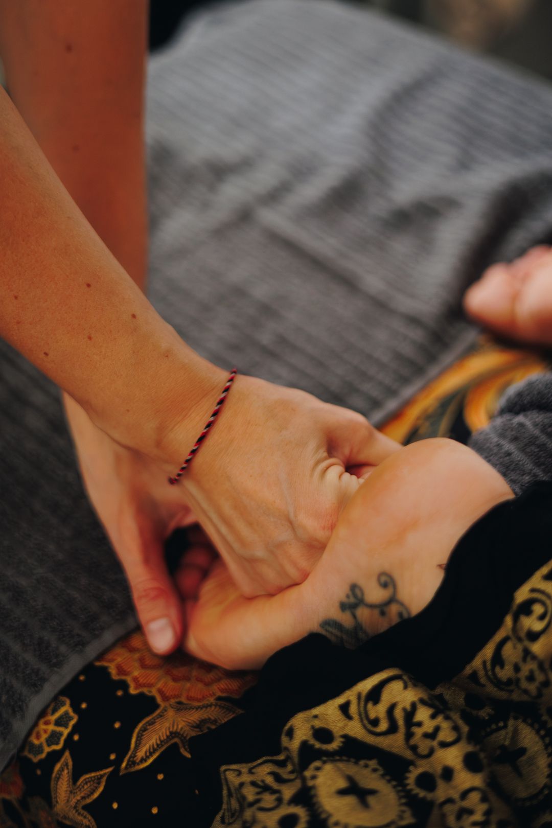 Therapist performing hand massage on client with tattoo and decorative blanket.