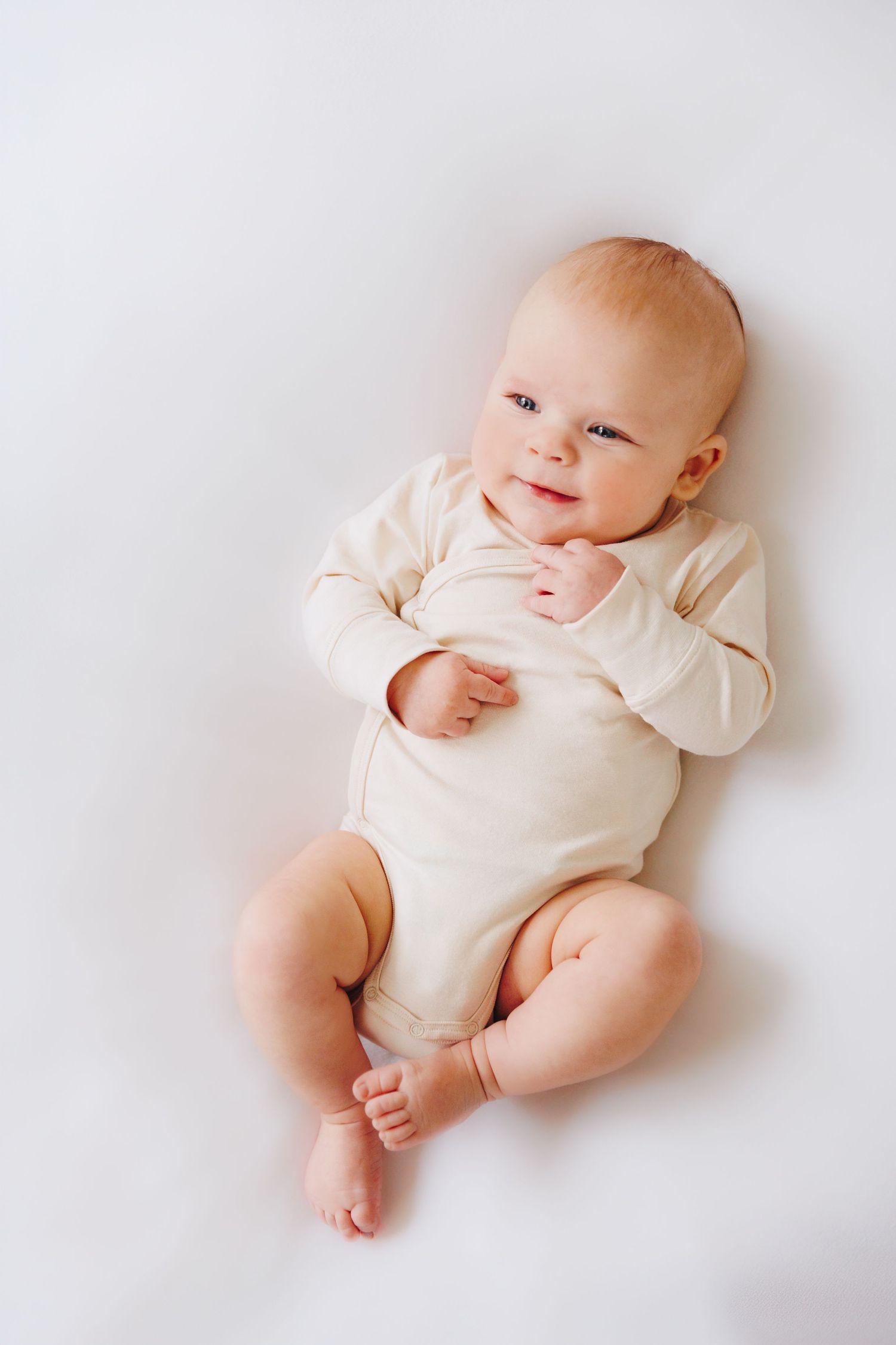 Smiling baby in cream onesie lying on white background.