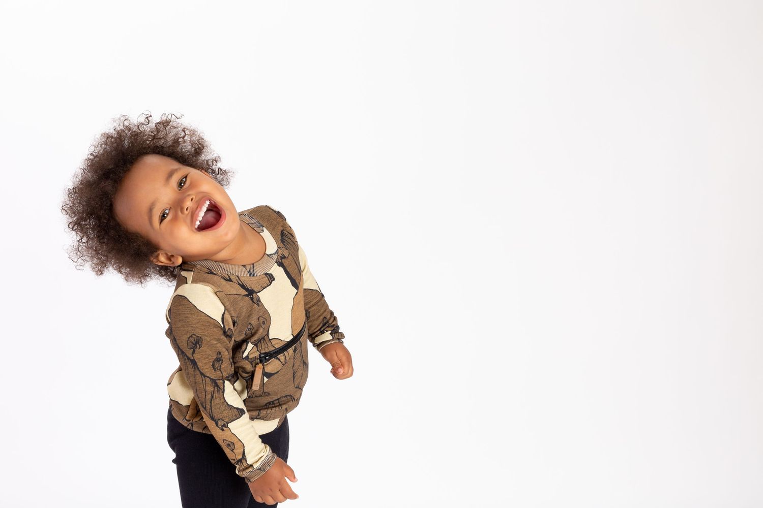 A young child wearing a brown jacket and blue jeans holds a delicate butterfly on their finger against a white background.