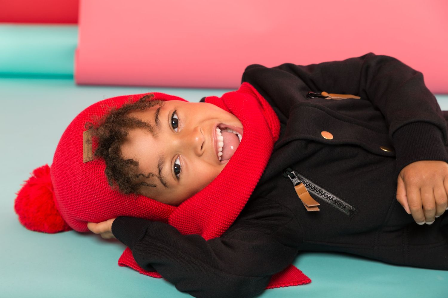 Person in a black jacket lying down on a pink and blue background in a sequence of five similar poses.