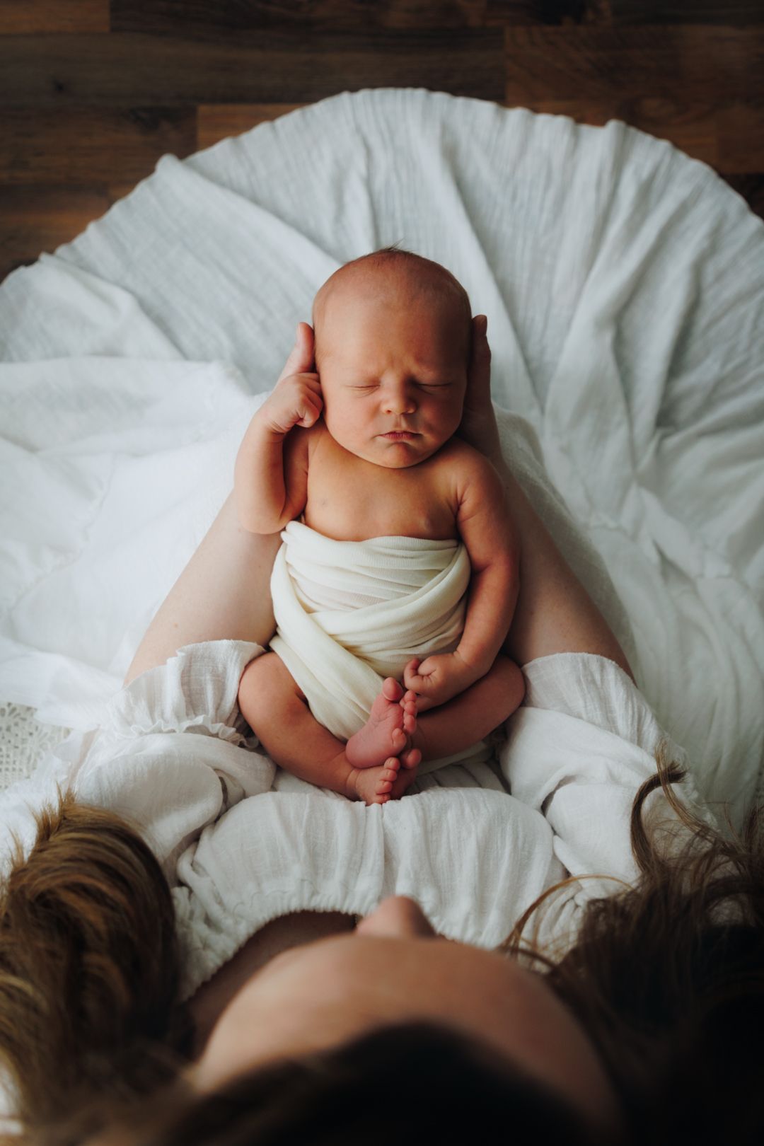 A peaceful newborn baby swaddled in white lies on soft bedding with natural light highlighting their delicate features.